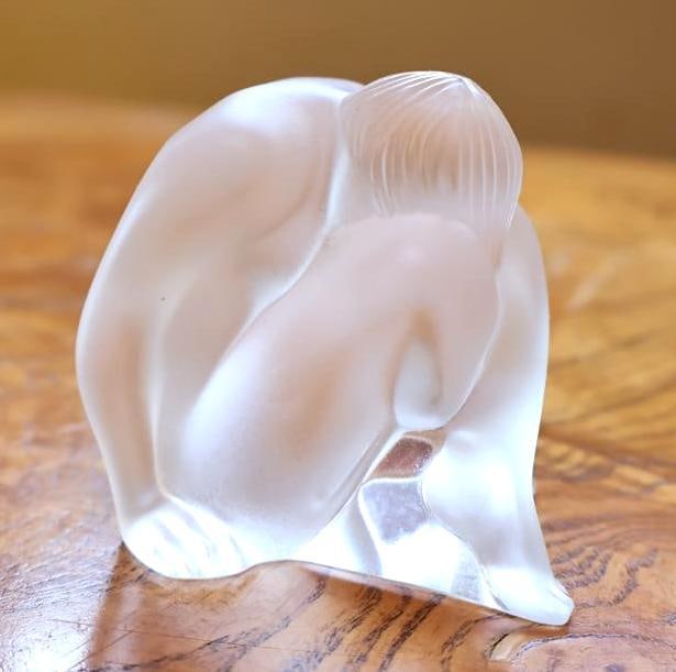 Lalique France Frosted Crystal Nude Female Figurine: Sculpted with flowing Art Deco-inspired lines, satin-frosted surfaces, and polished clear crystal accents. Signed Lalique France to the underside. Approx. 2"H x 2.5"H.