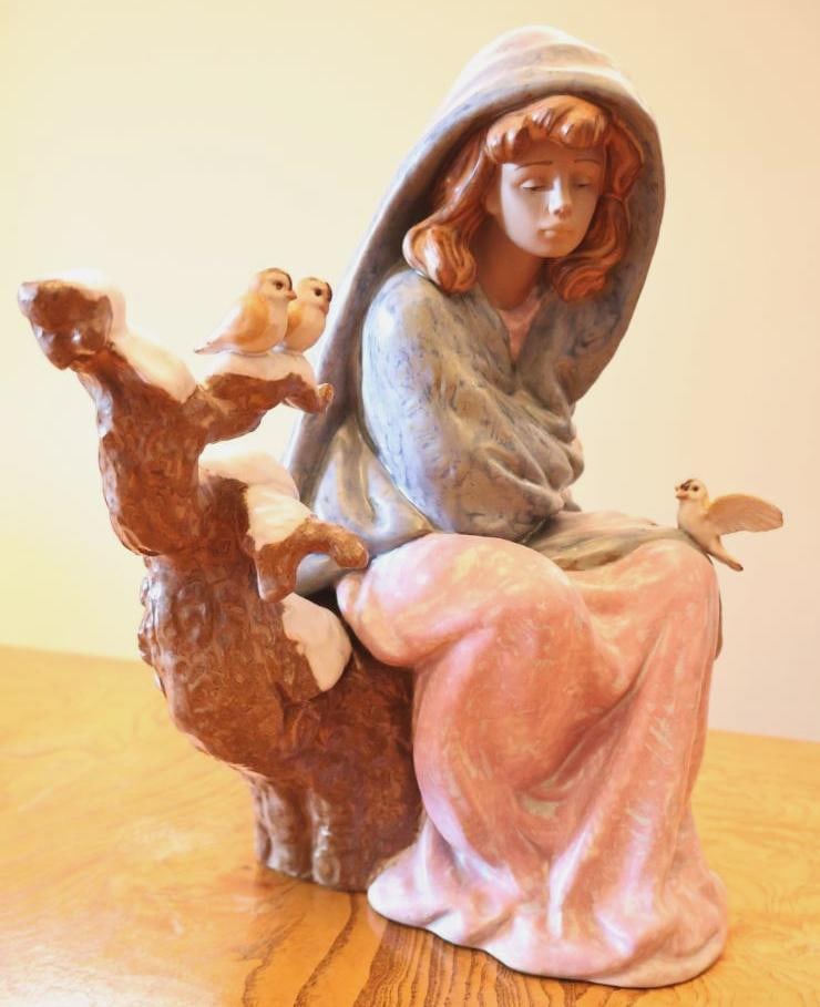 Lladro Winter Girl with Birds Porcelain Figurine: Large Lladro porcelain figurine, depicting a seated young woman bundled in a blue-gray hooded cloak and soft pink skirt, accompanied by several small birds perched nearby on a snow-covered branch.