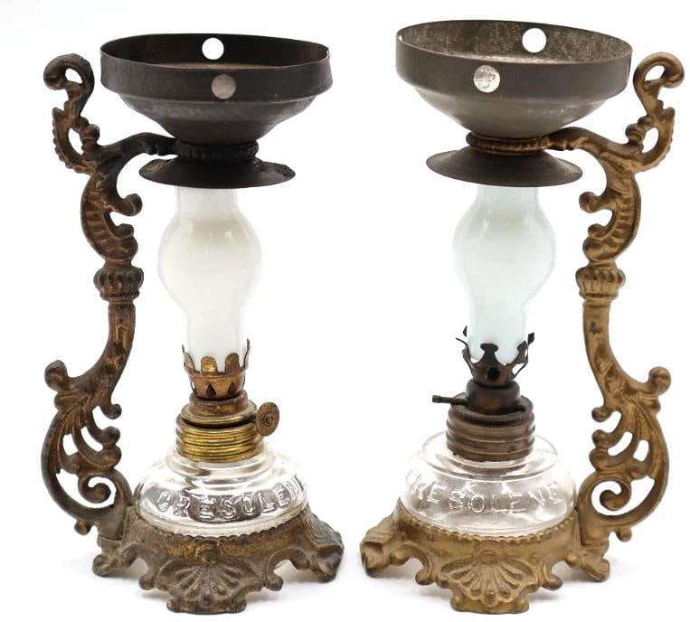 Pair Antique Cresolene Kerosene Nursery Lamps: Wonderful pair of antique CRESOLENE glass kerosene lamps mounted in ornate cast-metal bases with elaborate scrolling side brackets and upper reflector/shade holders. The clear glass fonts are boldly e