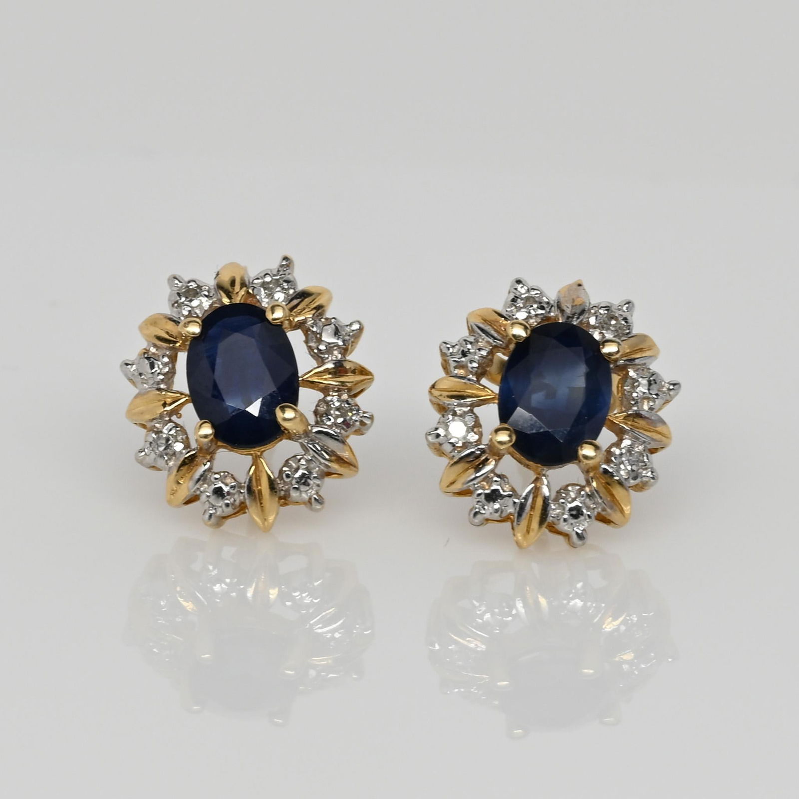 Blue Sapphire Diamond Cluster 14k Yellow Gold Earrings by Nissko: These exquisite Nissko-branded sapphire earrings showcase timeless elegance with their rich blue oval-cut sapphires at the center. Encircled by a stunning halo of brilliant diamonds and delicate gold