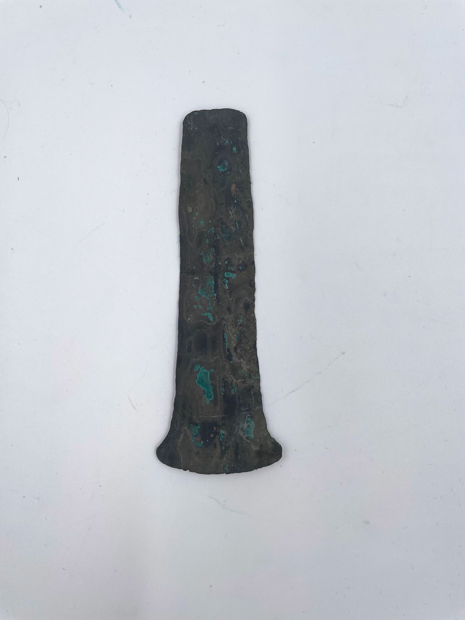 Ancient Copper Artifact: Offered here is a remarkable prehistoric copper artifact exhibiting a deep, aged patina with areas of green oxidation characteristic of ancient copper artifacts. The piece has a tapered form with a fl