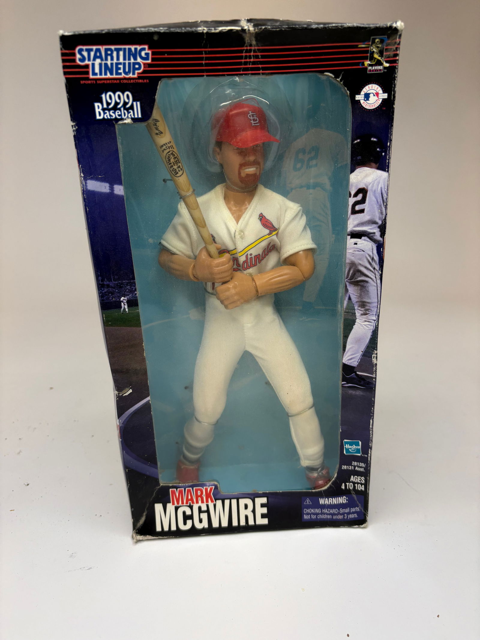 1999 Mark McGwire Unopened Posable Figure: 1999 posable Mark McGwire figure in original window box depicting a batter in a white St. Louis Cardinals uniform with red cap and printed Cardinals logo. The figure is posed gripping a wood-style bat