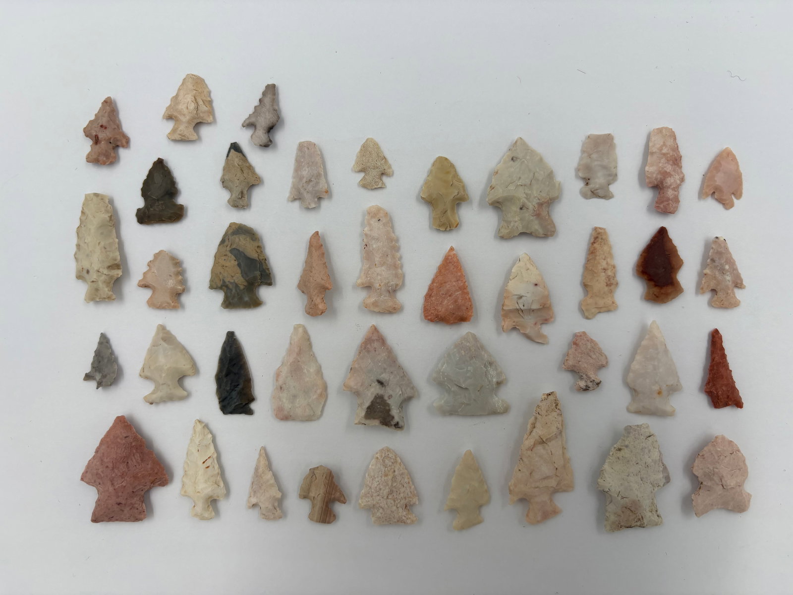 Collection of Fine Bird Points: Assortment of flaked stone projectile points in bird-point and triangular styles featuring stemmed, corner-notched and serrated forms. Colors range from pink and cream to gray, tan and red with