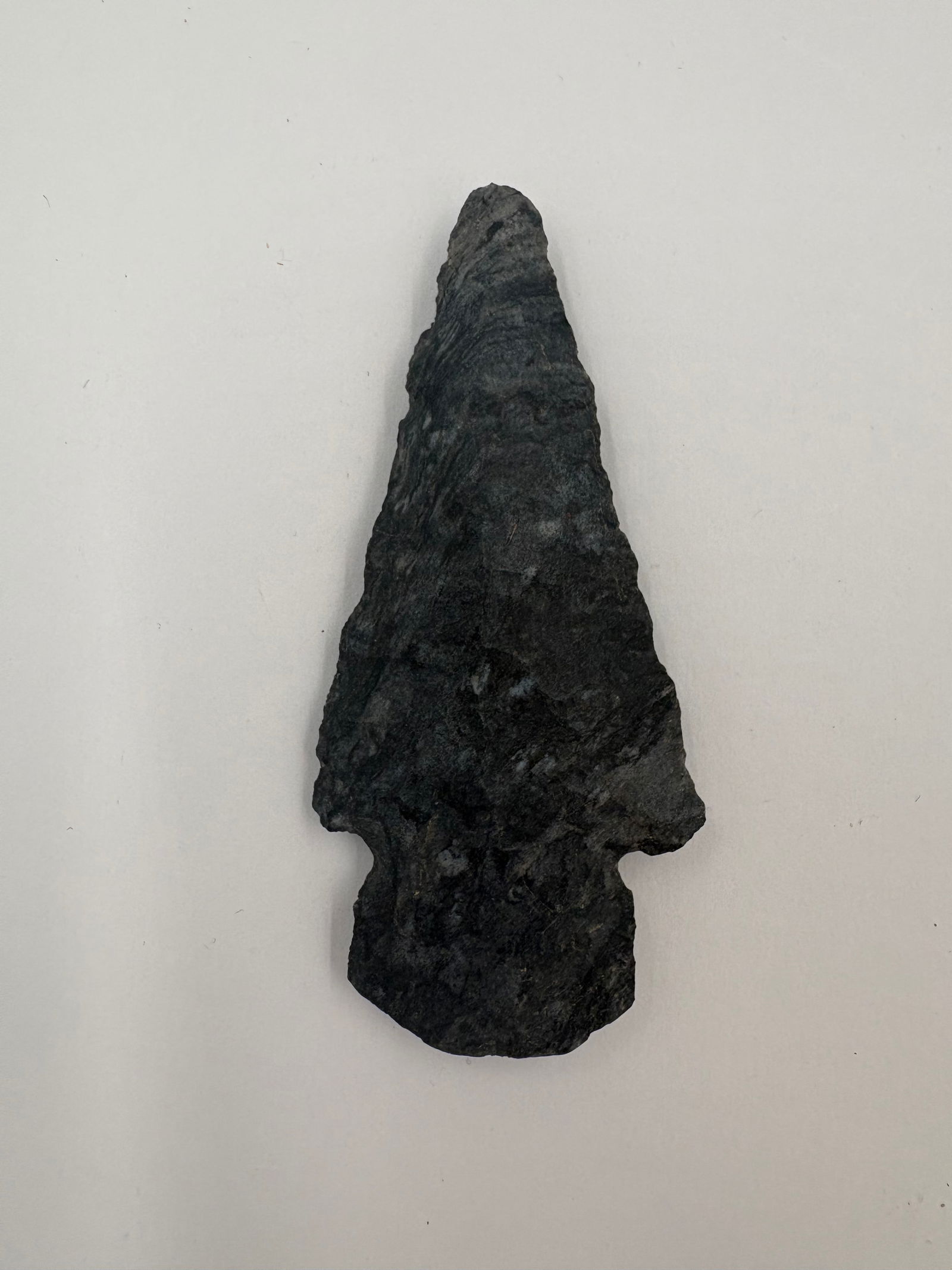 Dovetail - 3 1/4in: Dovetail-style projectile point measuring 3 1/4 inches, fashioned from black-and-blue striped chert. Dark charcoal to bluish-gray stone shows banding and lighter mottled inclusions across a