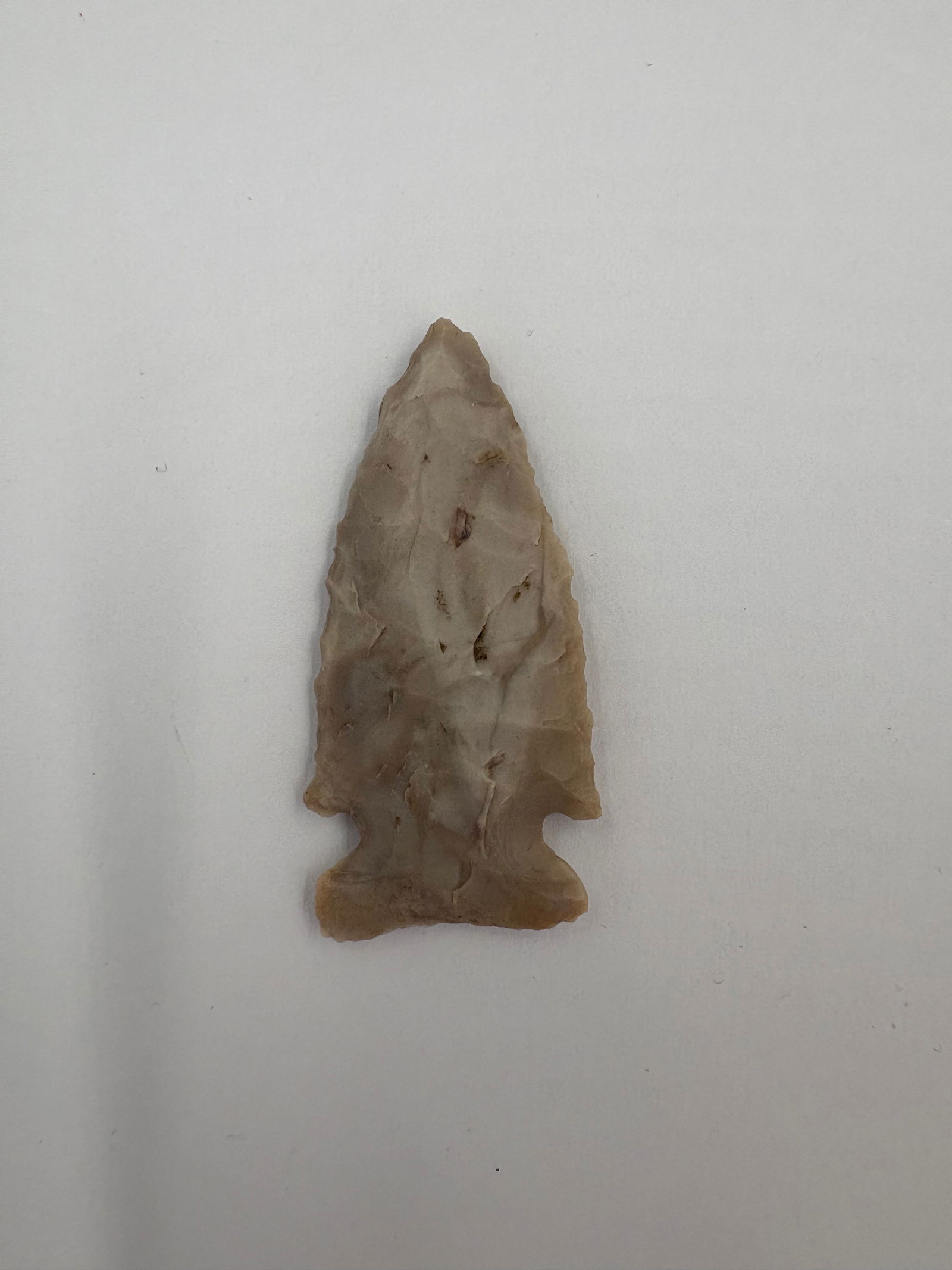 Colorful Side Notch - 1 3/4in: Side-notched projectile point crafted from fine-grained tan to beige stone with subtle gray banding. Tapered blade displays careful flaking and pronounced side notches that lead into a broad stemmed