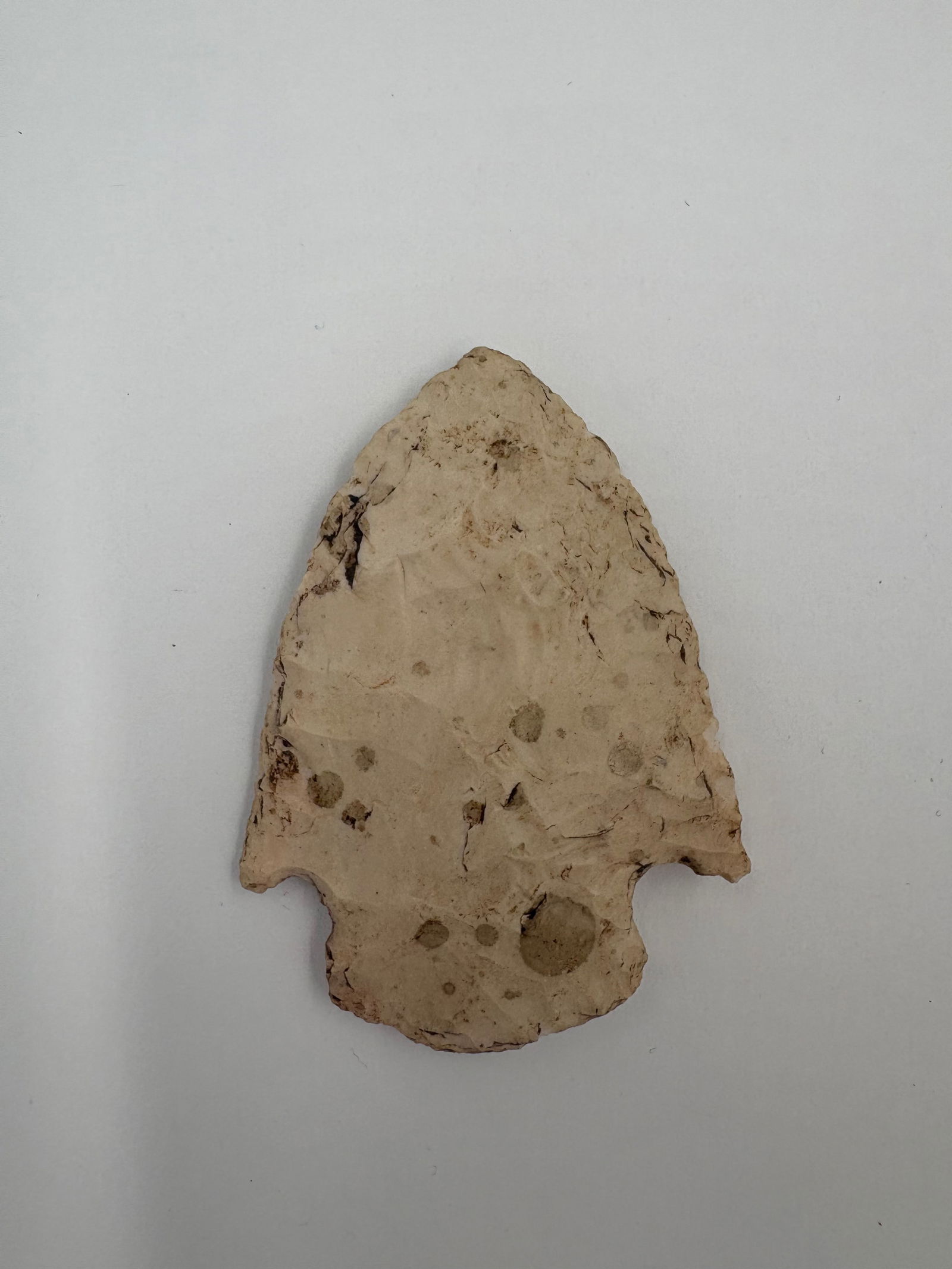 Snyder - 2 5/8in: Snyder-style projectile point measuring 2 5/8 inches, made from light tan stone with scattered gray inclusions. Bifacial flaking forms a broad triangular blade with a pointed tip and prominent basal n