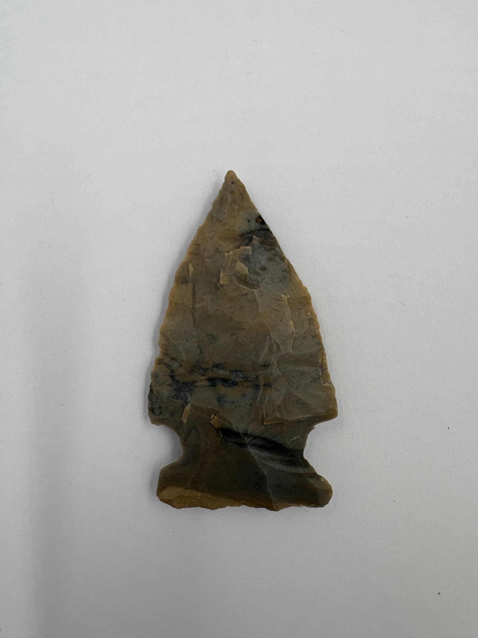 Cache River Point - 2in: Cache River-style point made of Reed's Spring chert, showing tan to olive-gray tones with darker gray banding. Narrow triangular blade with an acute tip and fine flake scars across both faces. Notched