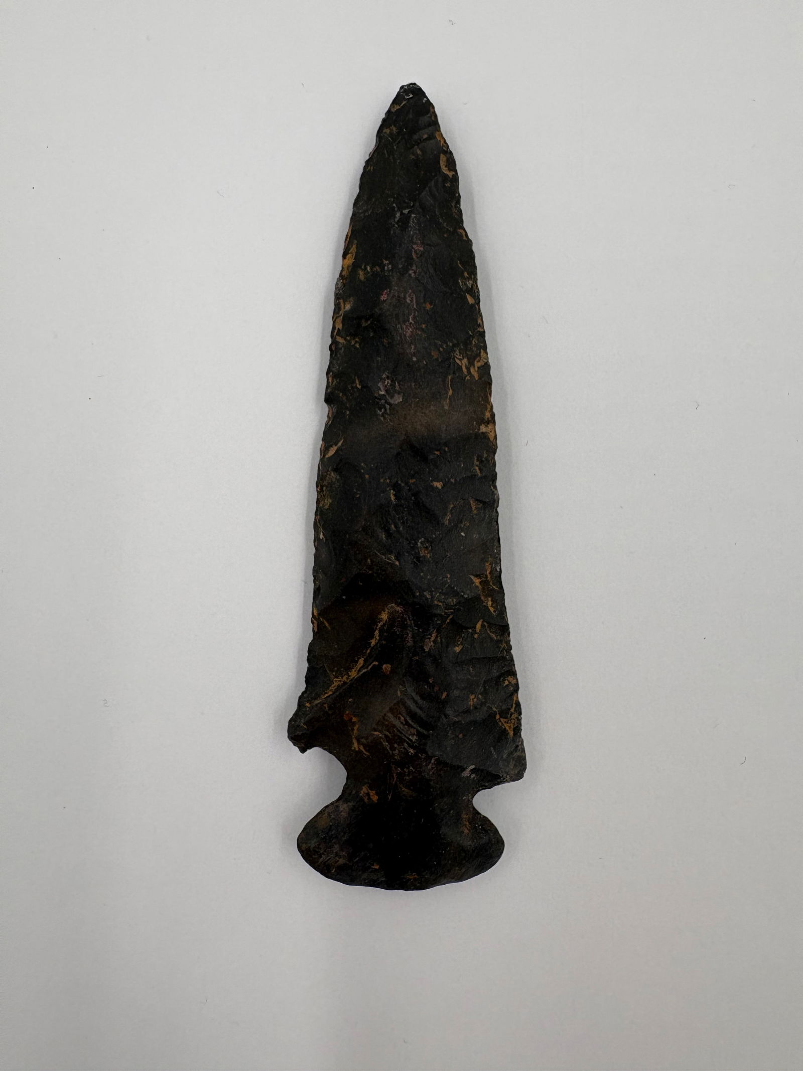 *Restored* Dovetail: Dovetail point fashioned from dark, flaked stone with pronounced bifacial percussion flaking along the blade. The piece narrows to a sharp tip and terminates in a broad dovetail base with prominent