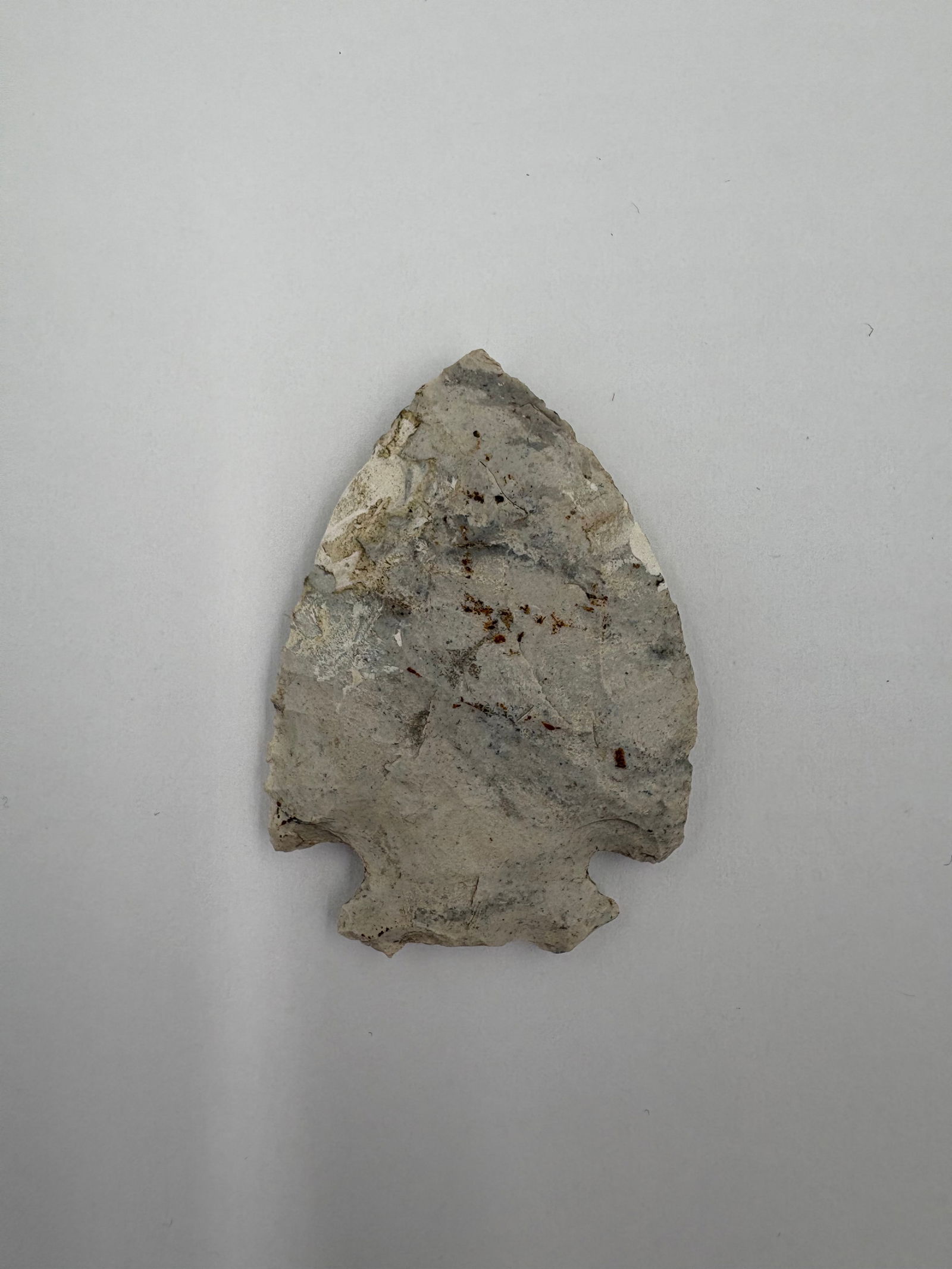 *Restored* Snyder: Restored Snyder-style stone projectile point measuring 2 in long. Light gray to cream coloration with visible flake scars and patches of residual cortex. Narrow triangular blade with a stemmed,