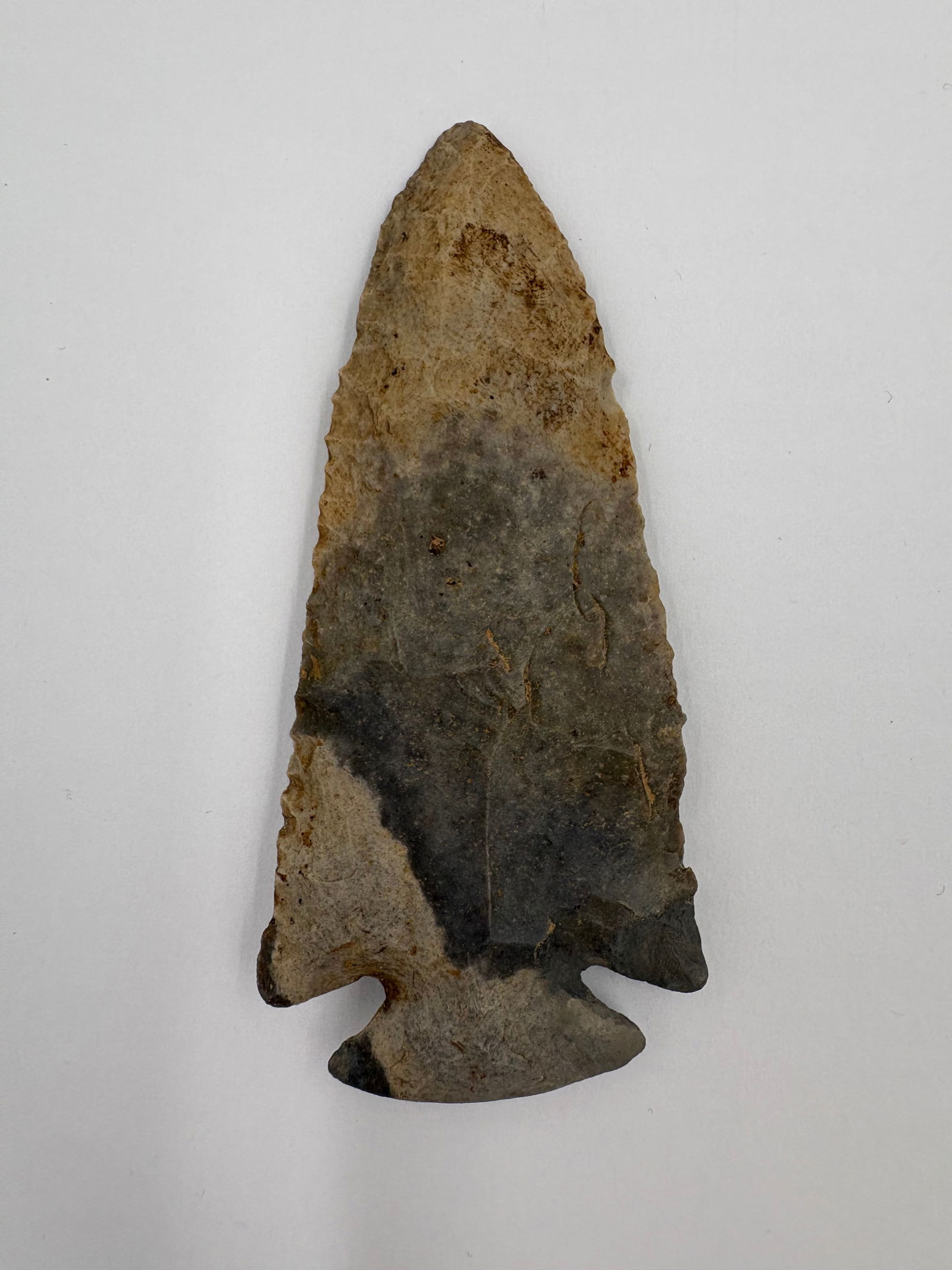 *Restored* Dovetail: Flaked stone dovetail point with a narrow, tapered triangular blade and a pronounced double-shouldered hafting base. Gray and tan coloration with darker patina patches and visible flake scars along