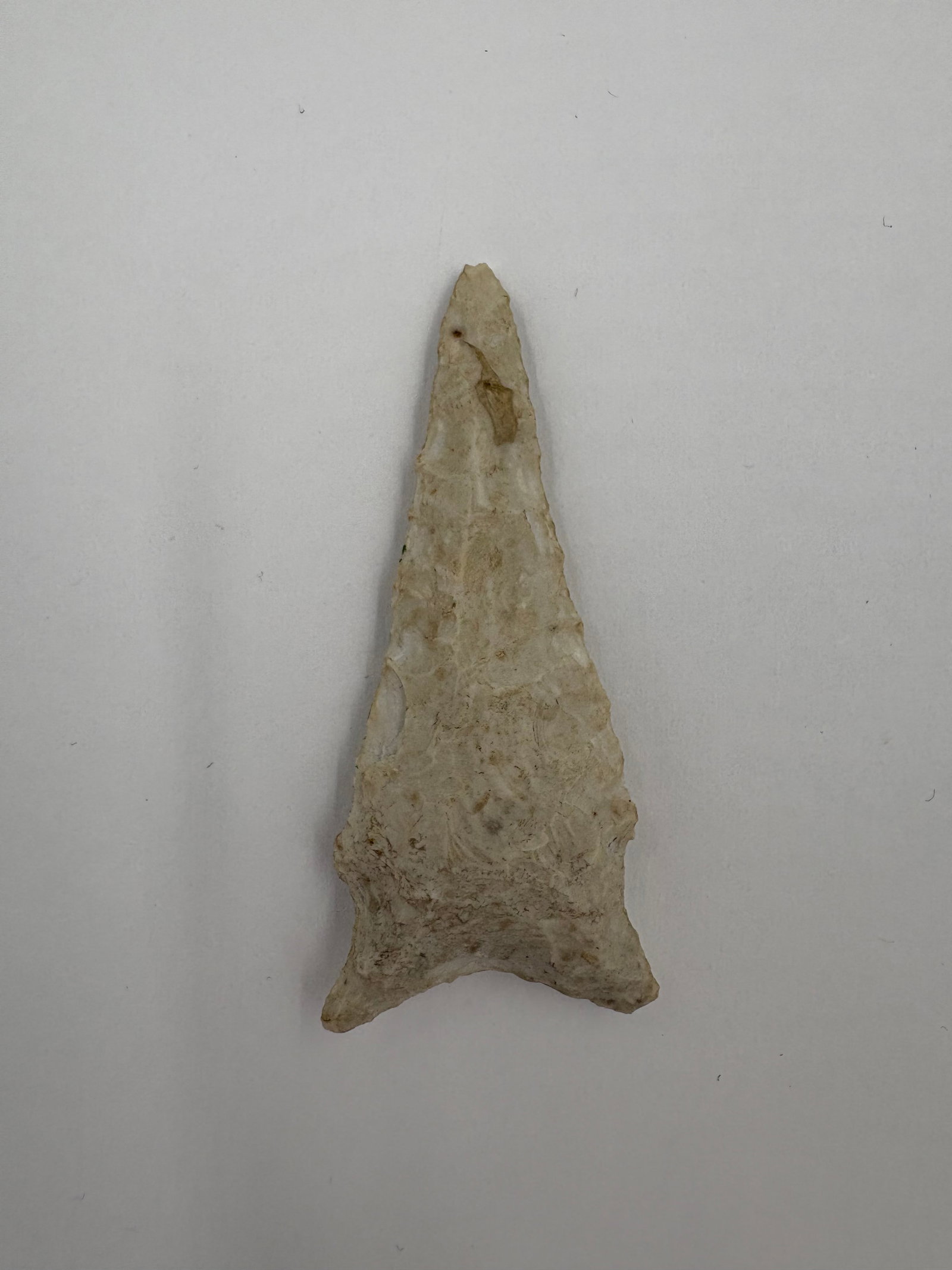 Hardaway Dalton: Light tan to creamy flaked stone point with a narrow triangular blade and pronounced basal projections. Bifacial flaking and edge retouch are evident across both faces, and one face has handwritten