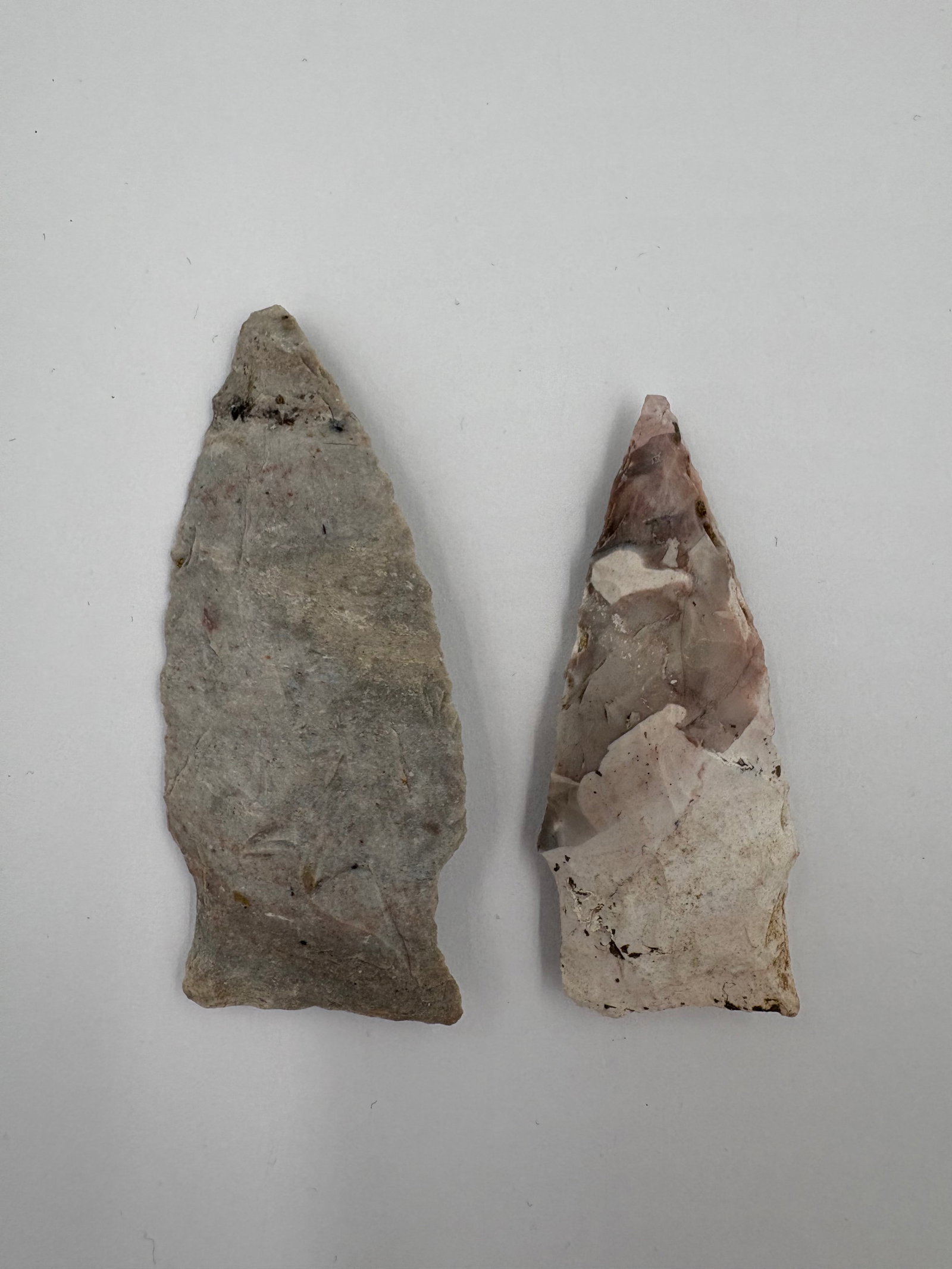 2 Rice Points: Two flaked stone Rice-style points exhibiting distinct materials and color zones. One example is a broad gray point with a slightly expanded stem base and subtle surface patina, while the other is a