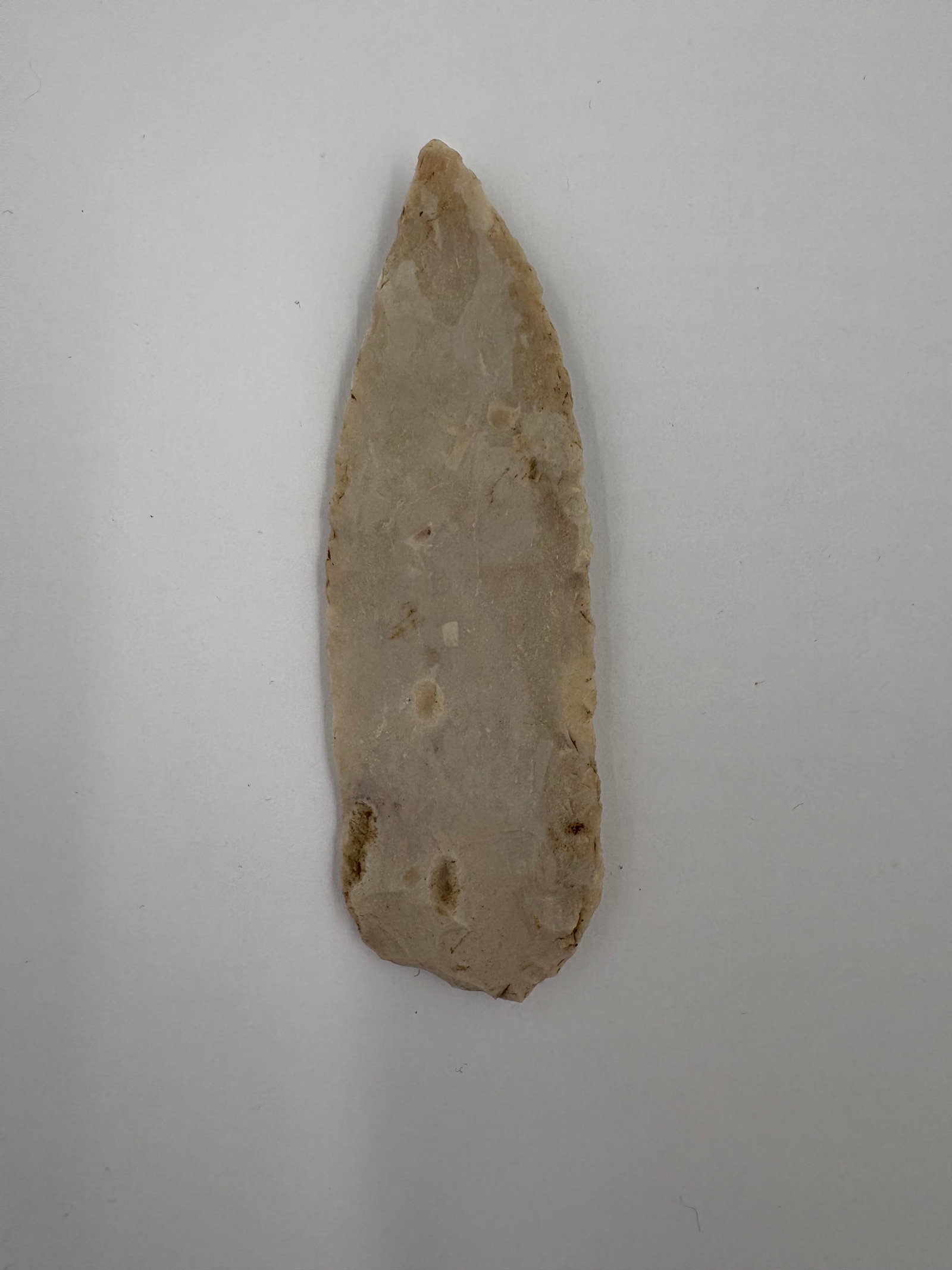 Sedalia: Elongated lanceolate flaked stone point measuring 3 3/4 inches with a narrow, tapered tip and a broader rounded base. Light tan to cream fine-grained stone exhibits bifacial flaking and small