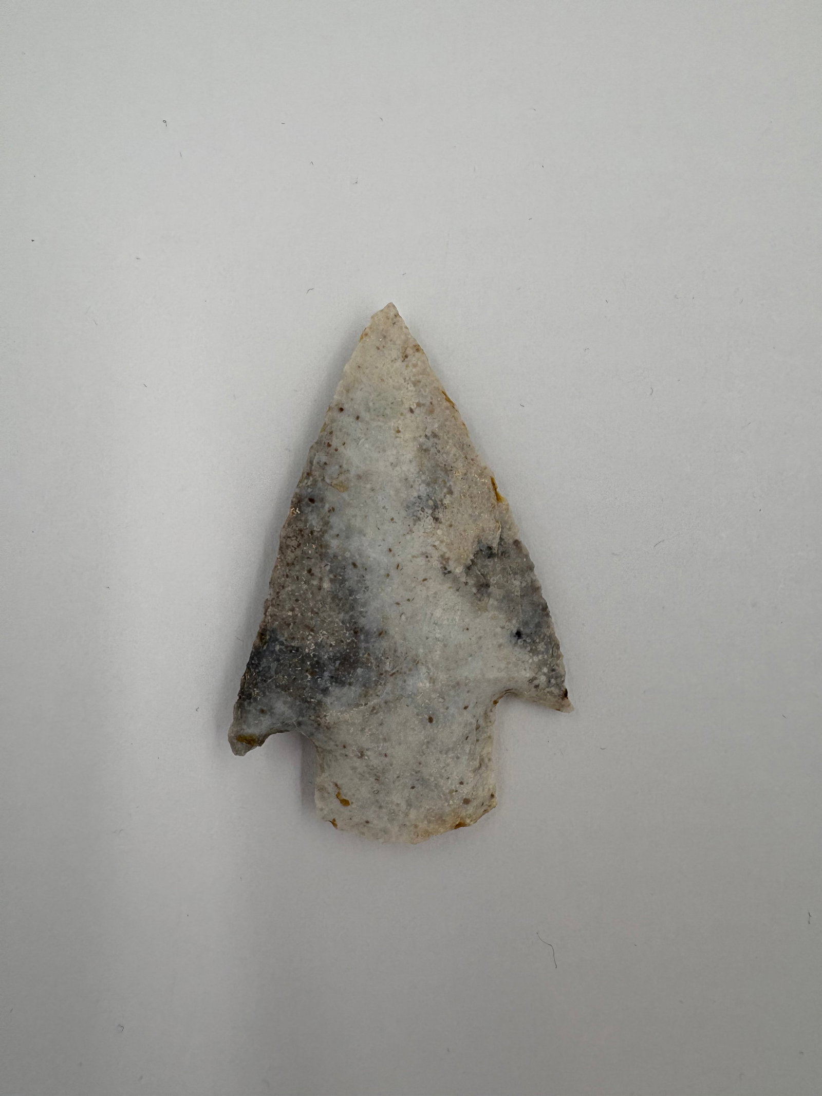 Kampsville: Light gray to white mottled stone projectile point with a broad triangular blade and distinct lateral notches near the base. Short stem with ear-like basal expansions and fine flake scars across both