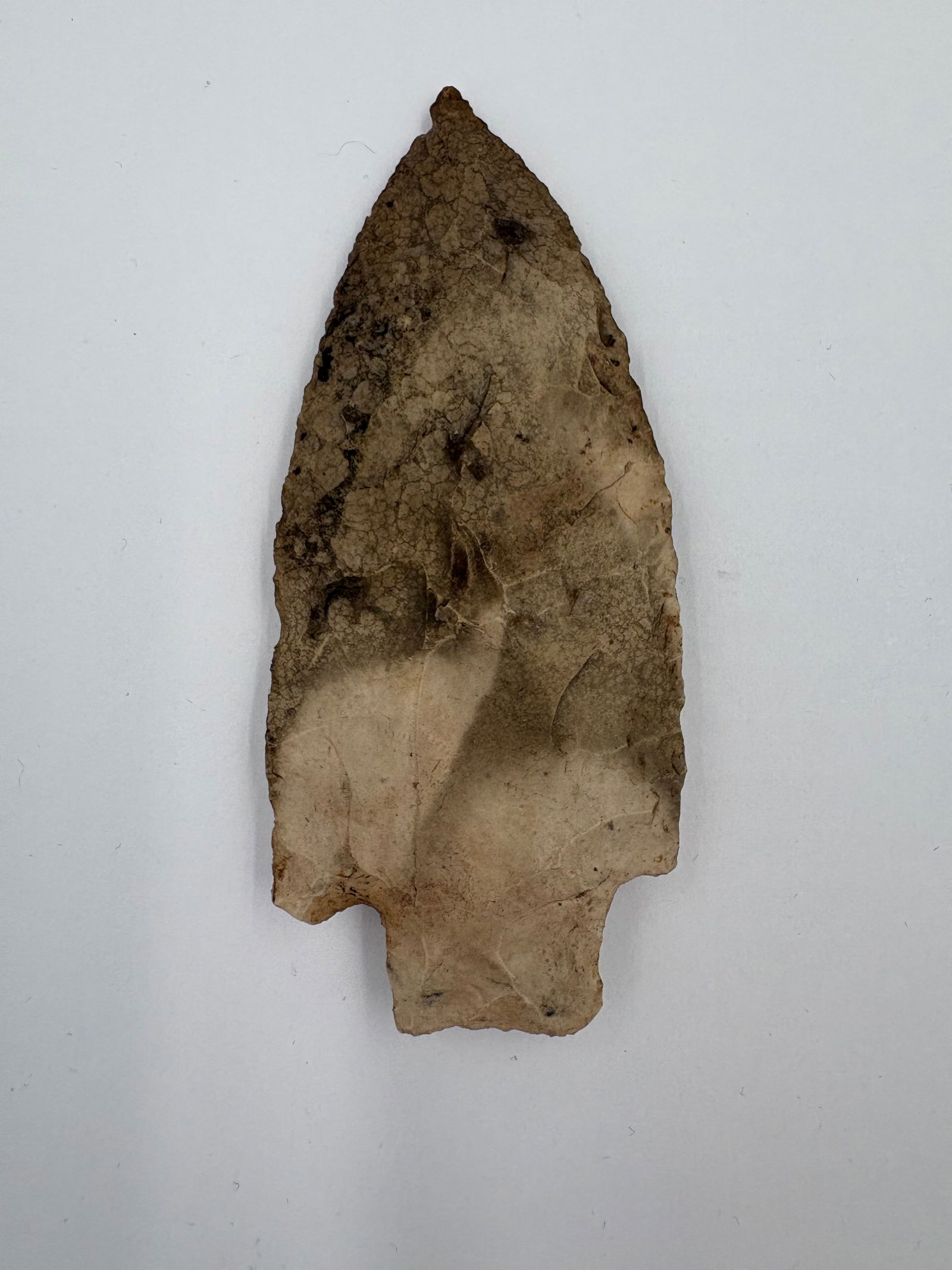 Etley: Etley-style flaked stone projectile point measuring 4in. Lanceolate blade with bilateral bifacial flaking and a notched stem base designed for hafting. Surface exhibits light tan to brown coloration w