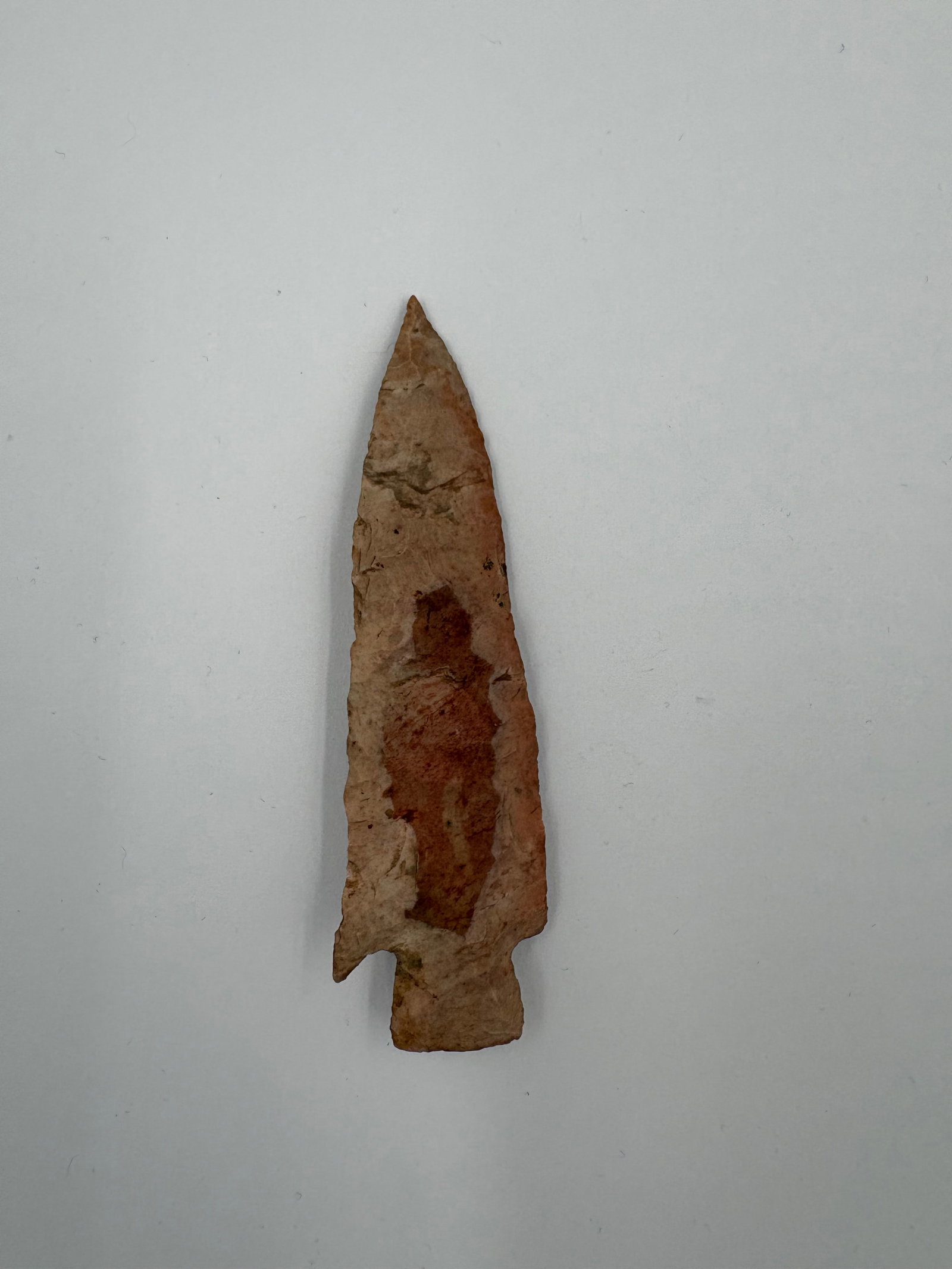 Etley: Flaked stone projectile point with an elongated triangular blade and a narrow stem featuring shallow basal notches. Surface shows tan to reddish-brown coloration with visible flake scars and bifacial