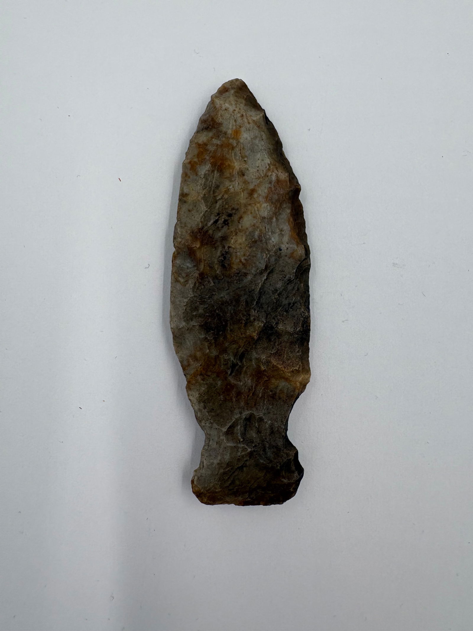 Matanzas: Matanzas-style stemmed projectile point crafted from gray-brown flaked stone measures 3 1/8 inches long. Tapered lanceolate blade with a defined stem and subtle basal ears displays bifacial flaking an