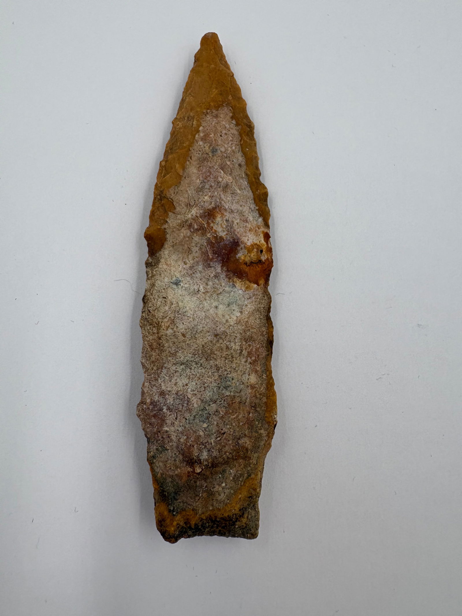 Creek-stained Etley: Etley projectile point fashioned from stone with a narrow, lanceolate profile and bifacial flake retouch along the margins. Surface displays pronounced yellow-orange creek staining with areas of