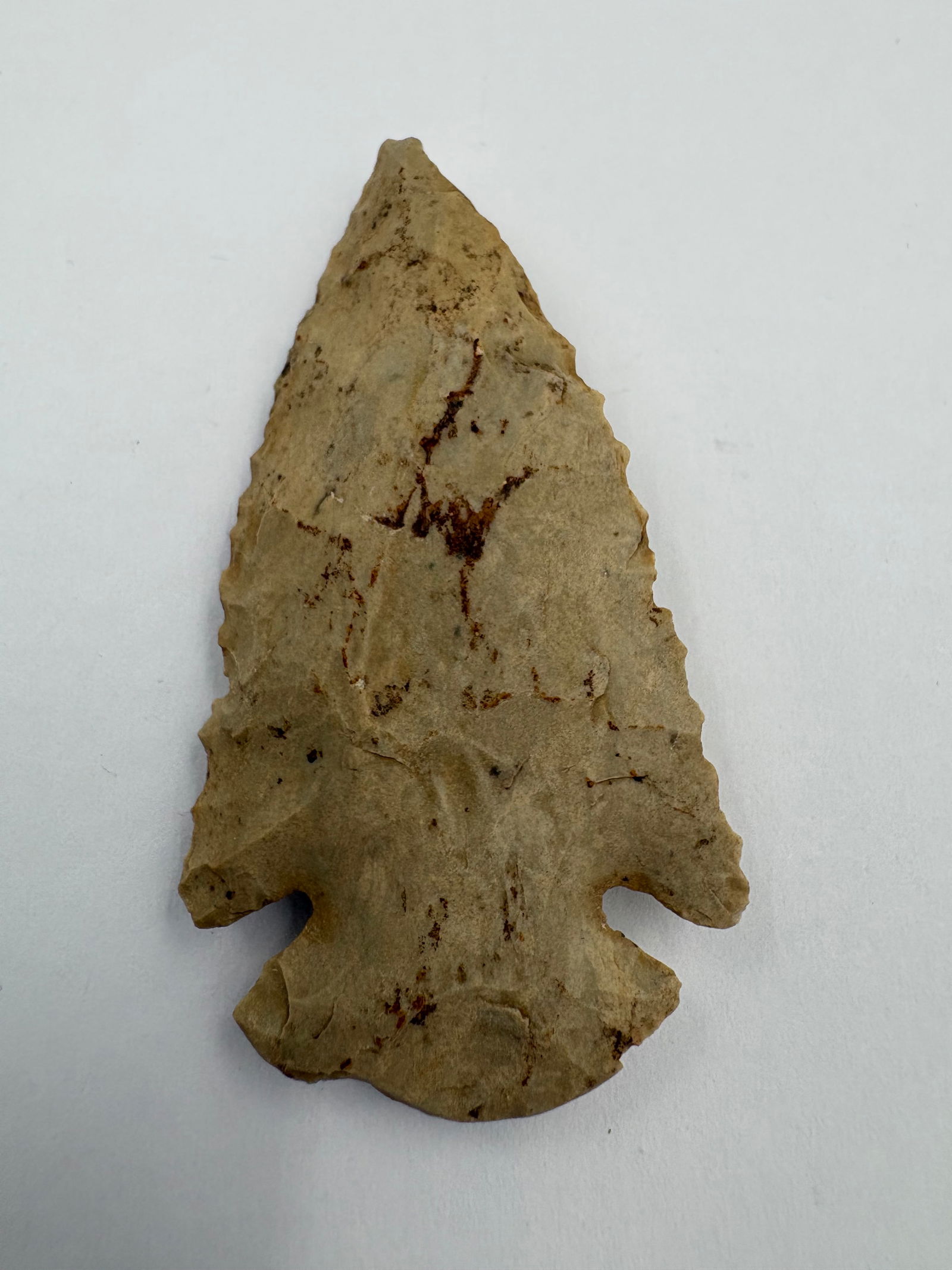 Dovetail: Dovetail-style flaked stone projectile point measuring 2 1/4 inches long. Beige-tan chert displays brown mineral staining and pronounced flake scars on both faces. Notched broad basal dovetail with