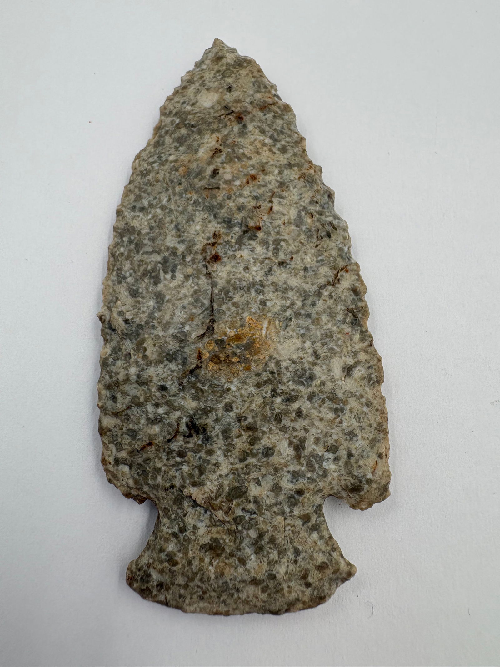 Dovetail: Dovetail-style projectile point measuring 2 7/8 in. Crafted from a gray-green speckled stone with small circular mineral inclusions, the piece has a thin, flat profile with bifacial flake scars along