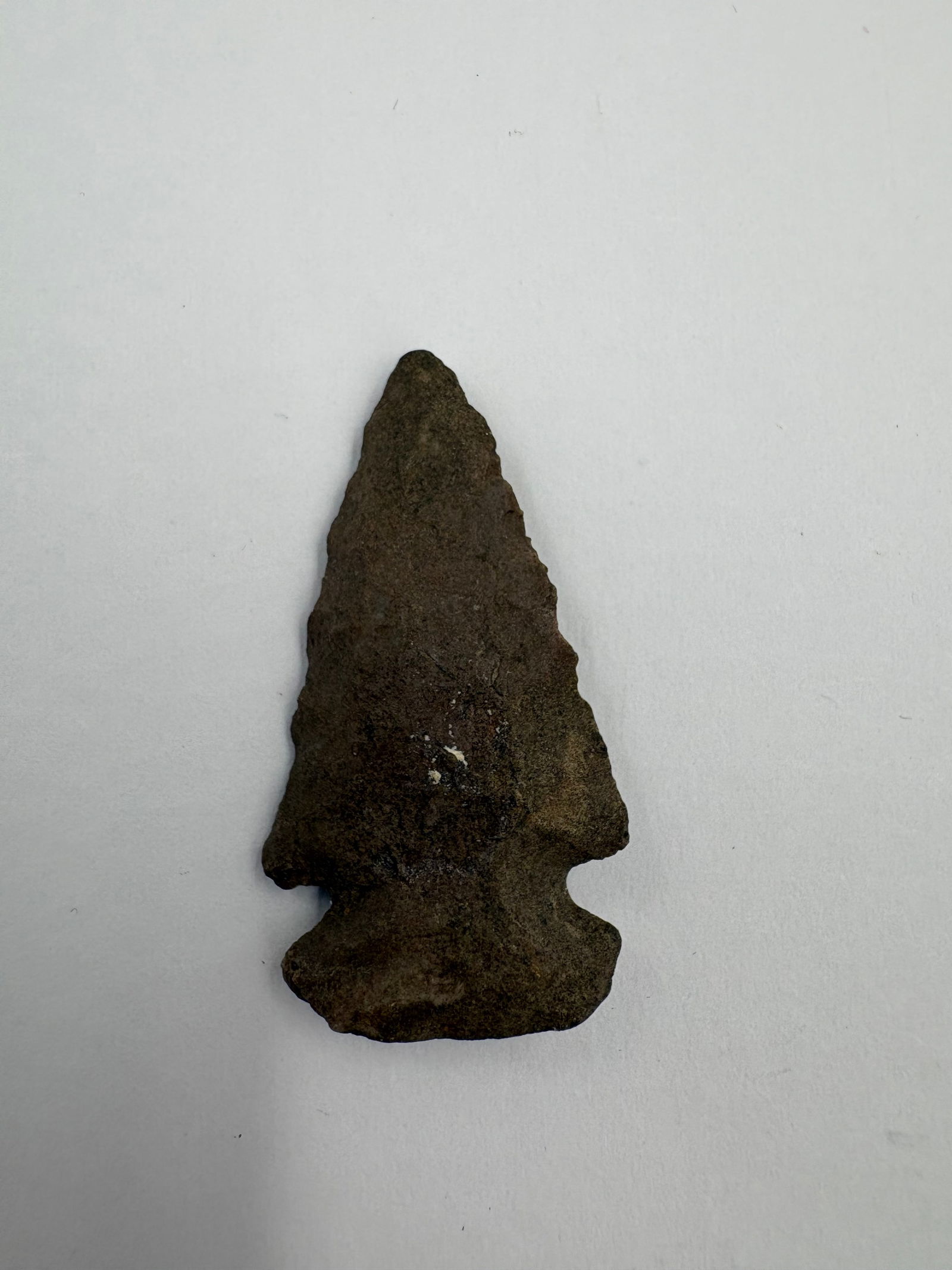 Dovetail: Dovetail-style stone projectile point with bifacial flaking and a dark brown-gray patinated surface. Broad basal ears and pronounced basal notches create a stepped dovetail outline, while the
