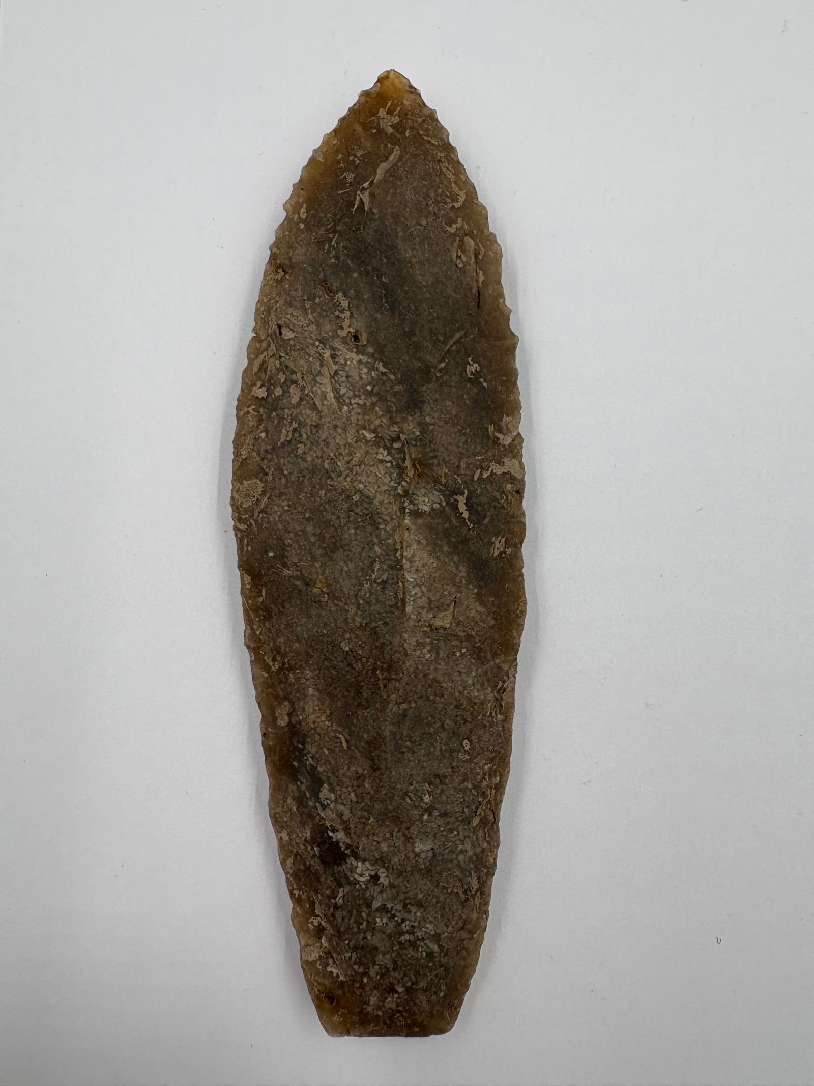 Sedalia, Sugar Quartz: Lanceolate sugar quartz point measuring 5 5/8 inches overall. Brown-gray translucent stone displays fine bifacial flaking with serrated margins, a sharply tapered tip, and a trimmed flat base.