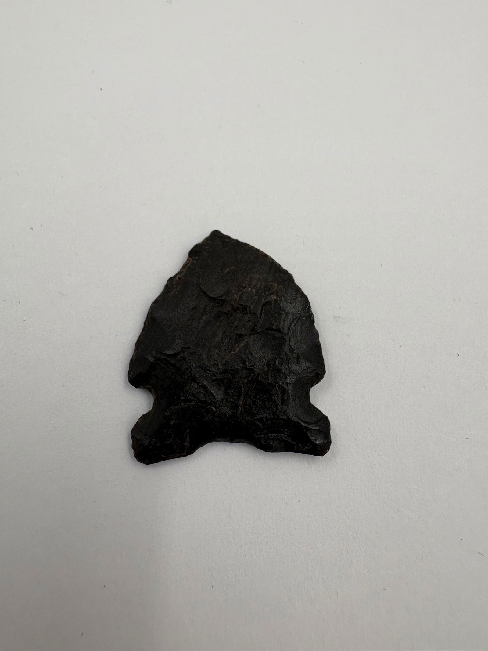Western Agate Point: Dark agate projectile point measuring 1 inch with a triangular blade and pronounced notched base. Hand-flaked surfaces display multiple flake scars and a thin, slightly beveled profile. Deep black to