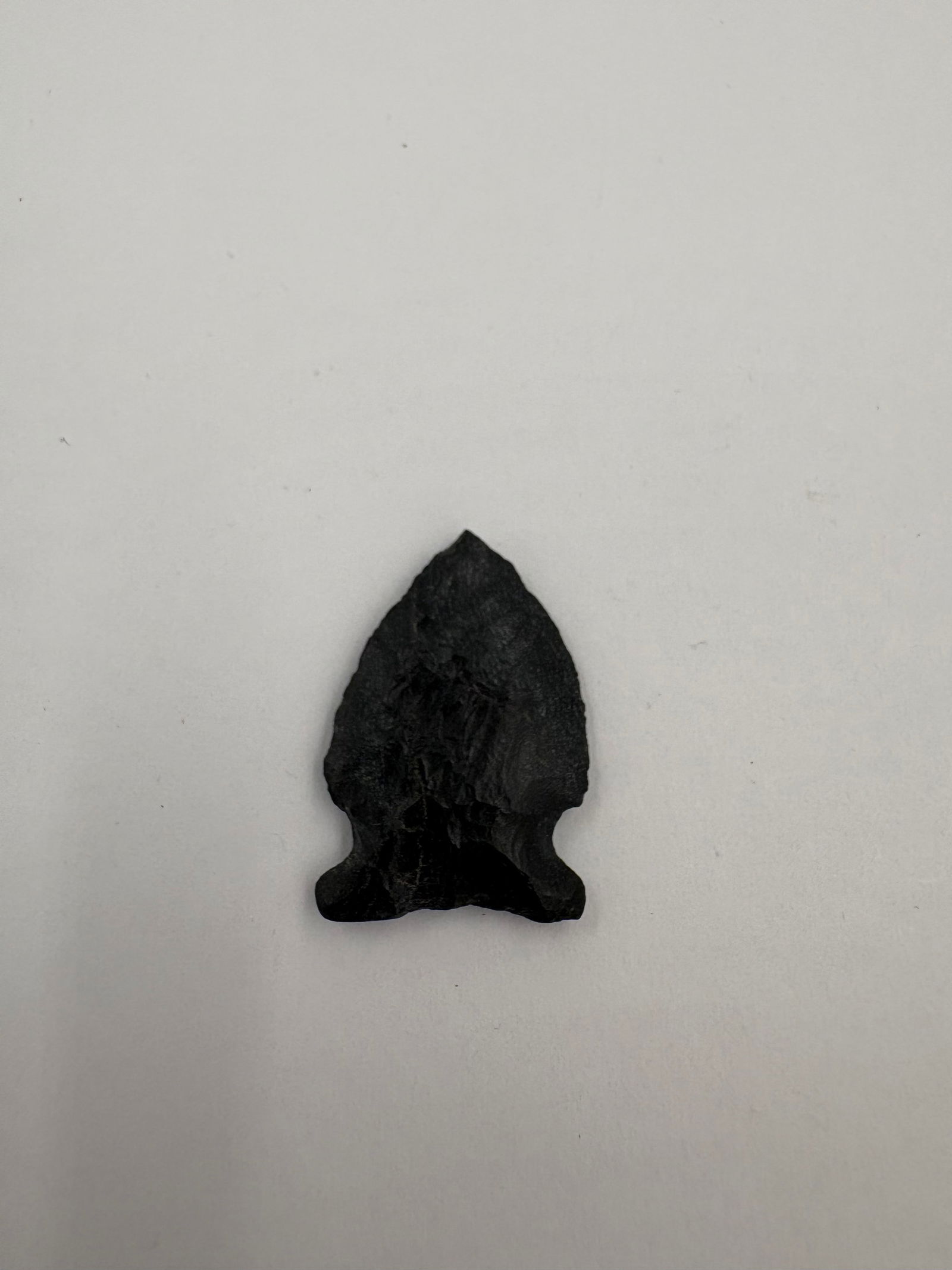 Western Agate Point: Black agate projectile point featuring pronounced bifacial flaking and a stemmed base with distinct basal notches. Thin, flat profile with well-defined flake scars across both faces and a tapered,