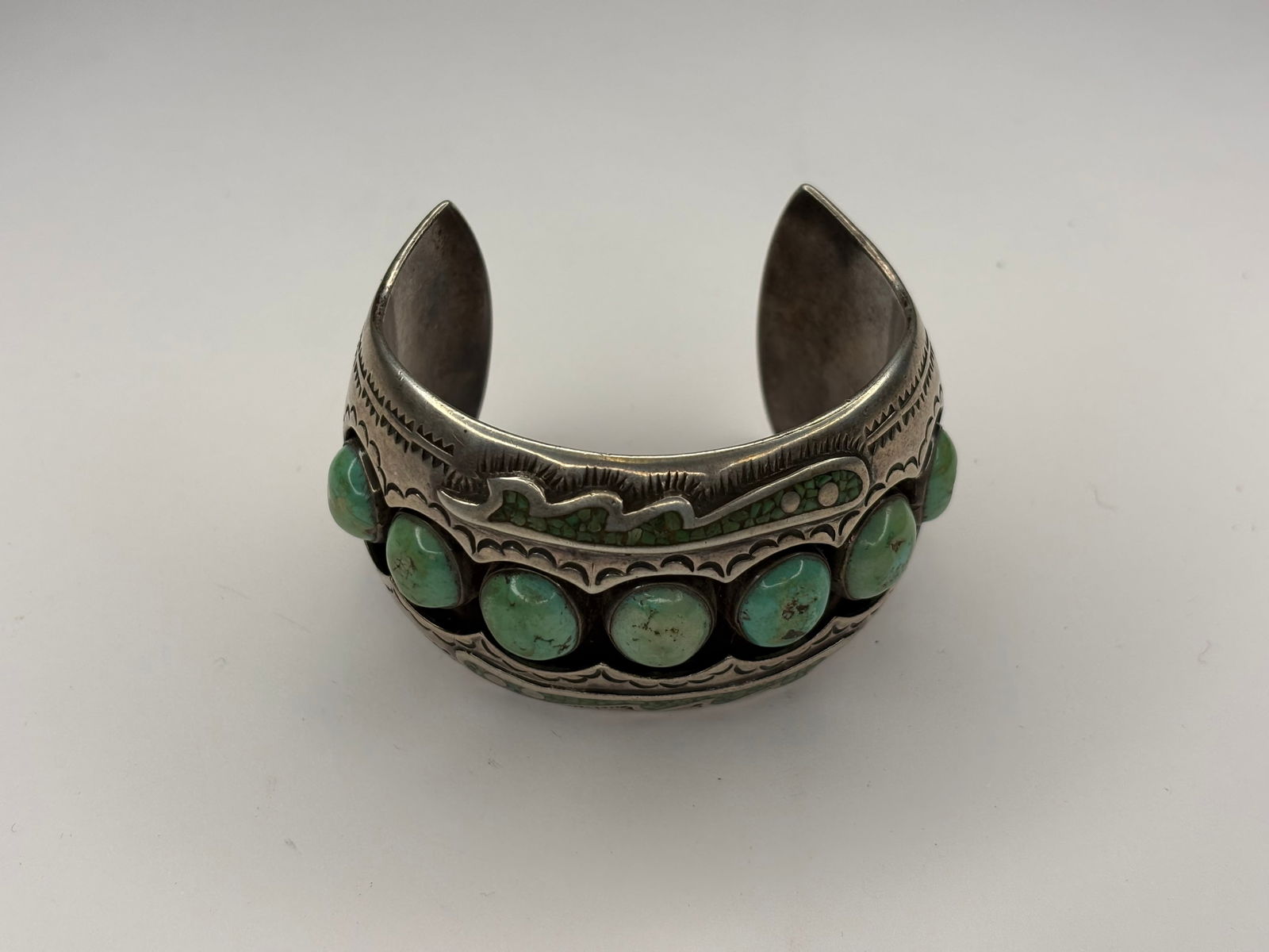 Primitive silver and turquiose bracelet, turn of the century: Wide silver cuff bracelet featuring a central row of round green-blue turquoise cabochons set in individual bezels with scalloped edges and narrow turquoise inlay accents. Band decoration includes