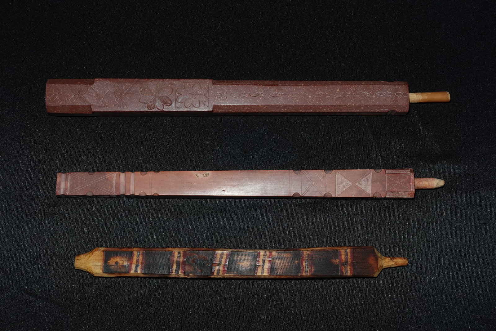 3 Sioux Pipestems: Three Sioux pipestems: two carved catlinite stems and one painted wooden stem. The catlinite pieces are reddish-brown, rectangular in profile with incised floral and geometric motifs, notched edges
