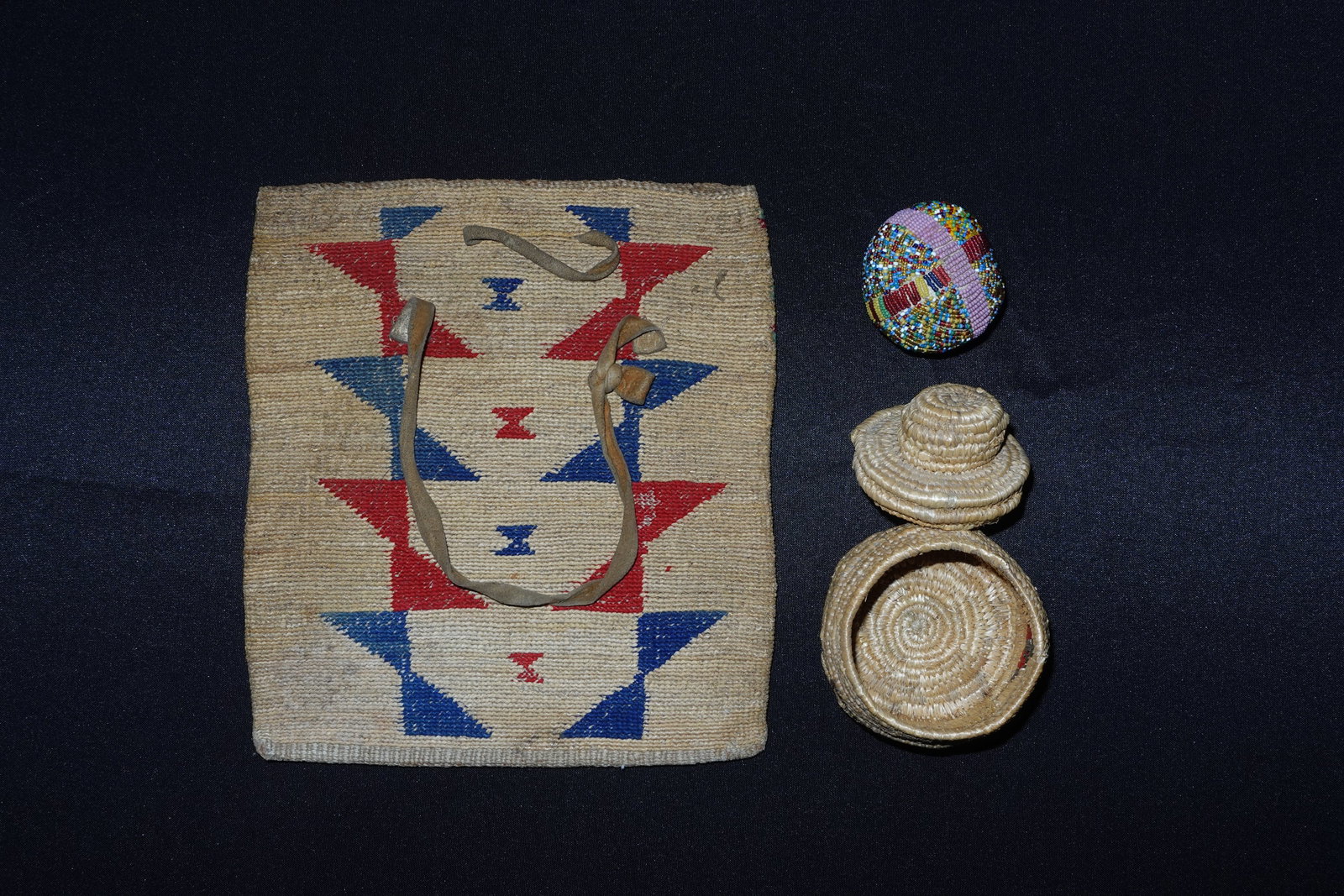 Cron Husk bag, Beaded Ball, basket: Nez Perce cornhusk bag woven in a flat rectangular form with repeating geometric triangular and band motifs in red, blue and green. A narrow leather strap threads through the upper edge and the body