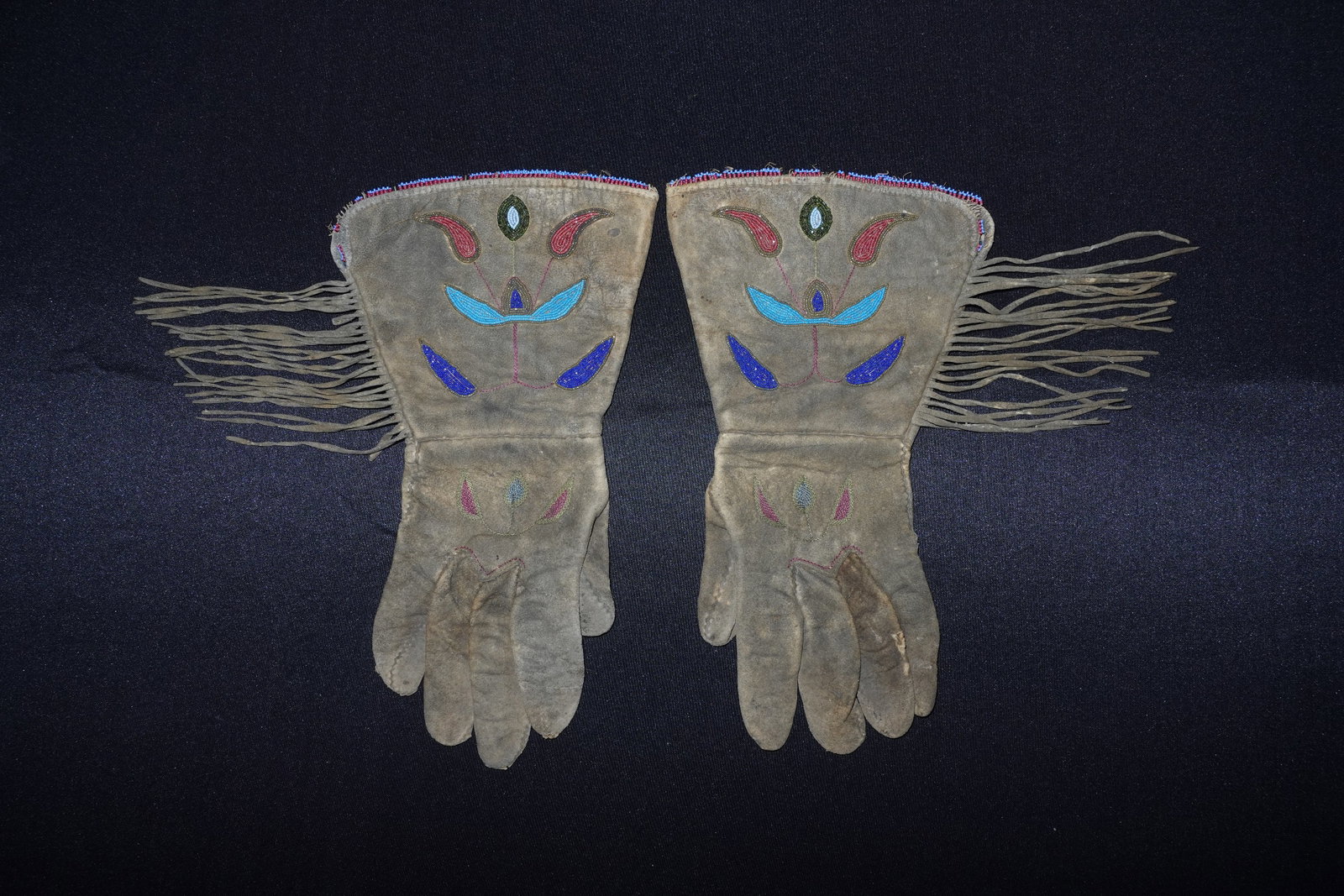 Early Modoc Bow: Gauntlet-style leather gloves with extended cuffs decorated with floral beadwork motifs. Cuffs display blue, red and green seed-bead appliqu?s and a narrow multicolor beaded edging, with long leather 