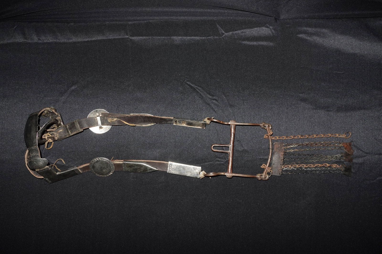 Vintage Bridle with Silver Adornment: Leather bridle with large oval and tapered rectangular silver-tone mounts and decorative conchos along the brow and cheek straps. Brown leather exhibits surface wear, creasing, and old stitching