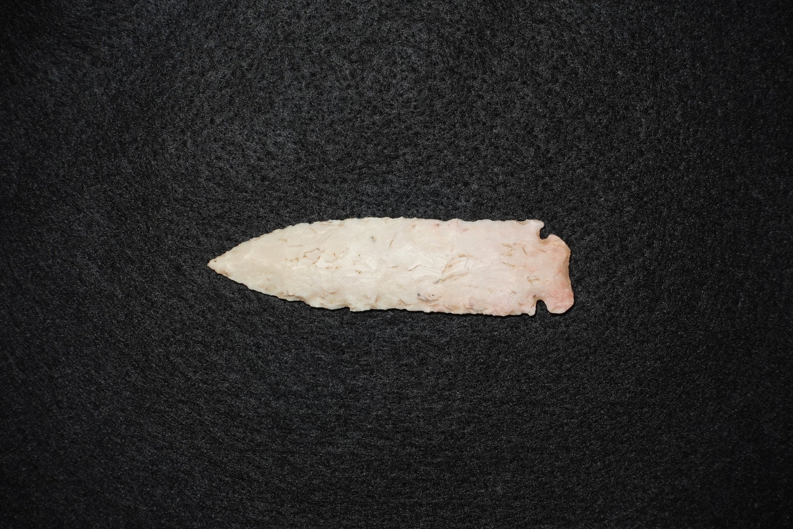 Howard County: Elongated bifacially flaked white stone projectile point with a slender lanceolate blade and tapered tip. Creamy-white to pale pink coloration shows brown mineral streaks and subtle translucent areas