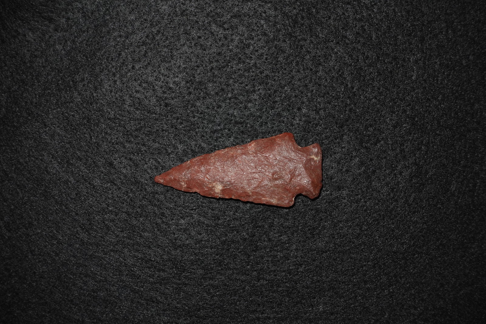Kirk - Red Hixton: Reddish-brown flaked stone projectile point with an elongated triangular blade and a pronounced basal notch. Bifacial flaking along the blade and a slightly crushed tip indicate deliberate knapping,