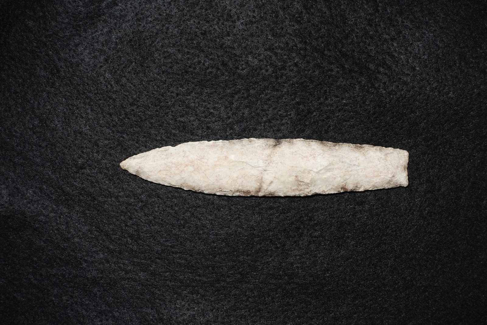 Sedalia: Long leaf-shaped projectile point fashioned from light tan to off-white stone with bifacial flaking and a pronounced central ridge. Blade edges show fine flake scars and the distal end tapers to a