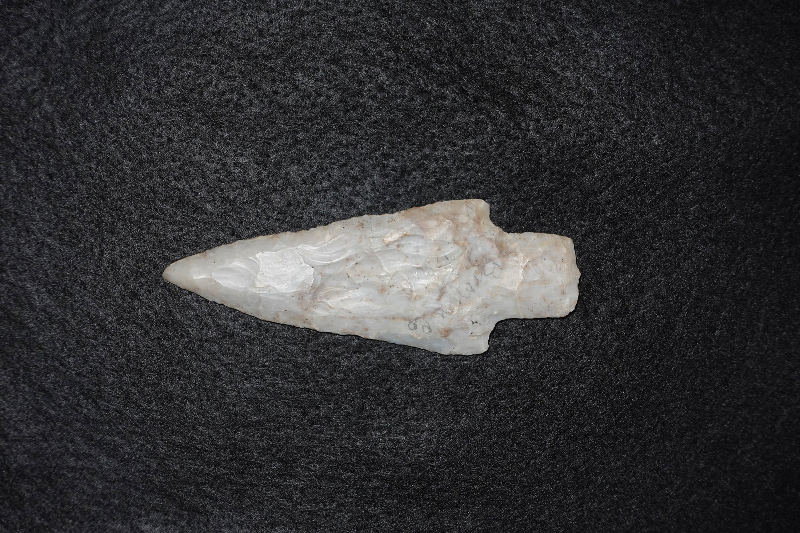 Adena: Elongated flaked stone projectile point with a tapered triangular blade and a slight stemmed base. Made from milky translucent chert/quartz with prominent concentric flake scars on both faces and