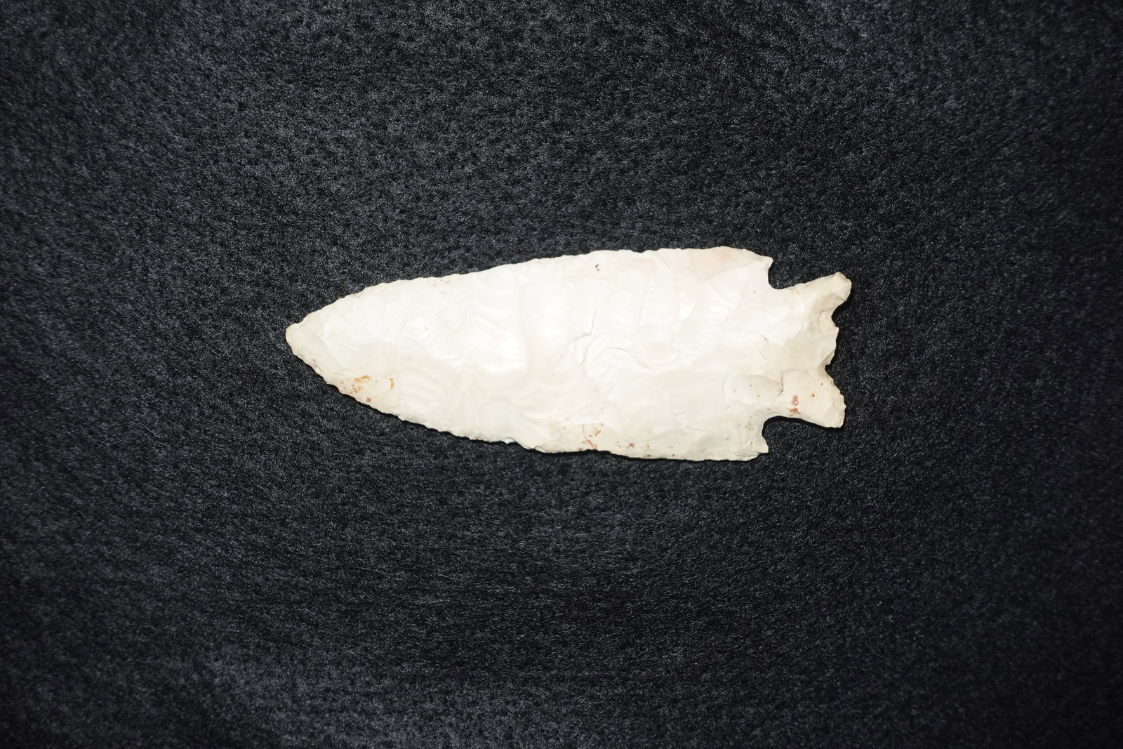 Stillwell: Cream-colored chert projectile point with extensive bifacial flaking and a stemmed, notched base. Fine pressure-flake scars create a smooth, reflective surface across the blade faces. Small
