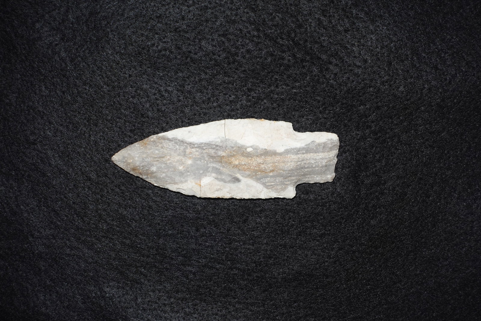 Kramer: Lanceolate bifacially flaked chert point with a narrow, leaf-shaped blade and a subtle basal notch. Translucent white to light gray banding runs along the surface with areas of rust-colored mineral