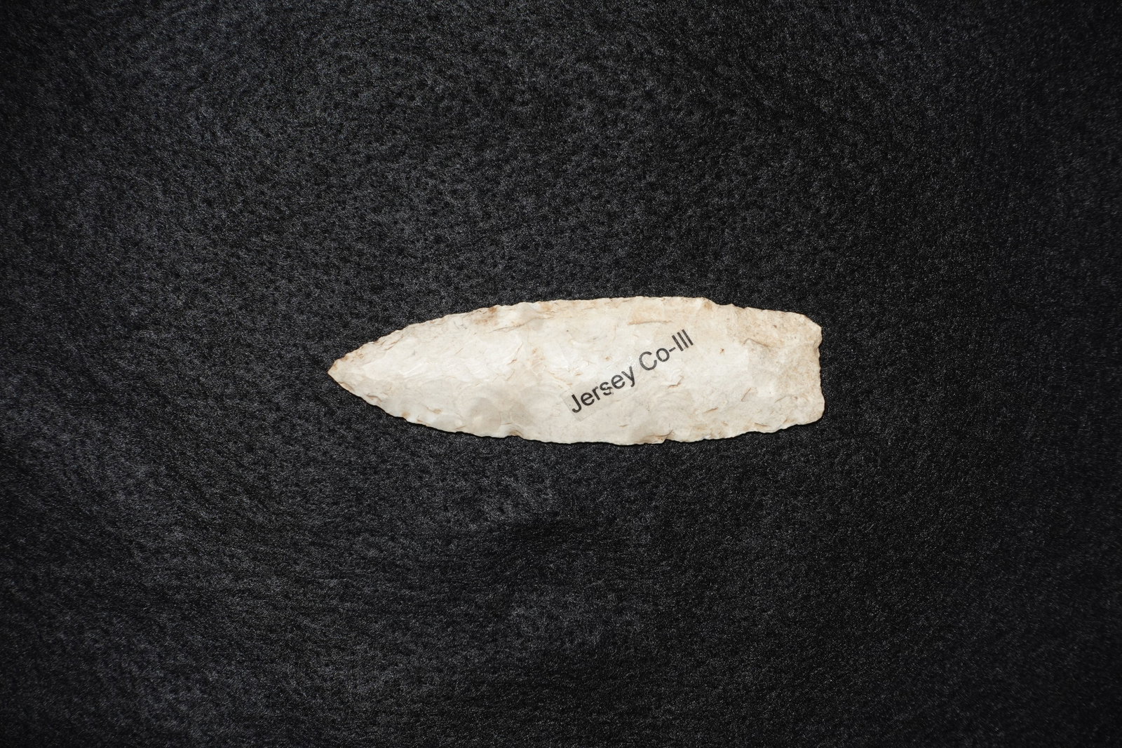 First View: Lanceolate bifacial flaked point crafted from pale cream to off-white chert with a tapered tip and broad straight base. Fine pressure flaking along both faces creates serrated-edge detail and the