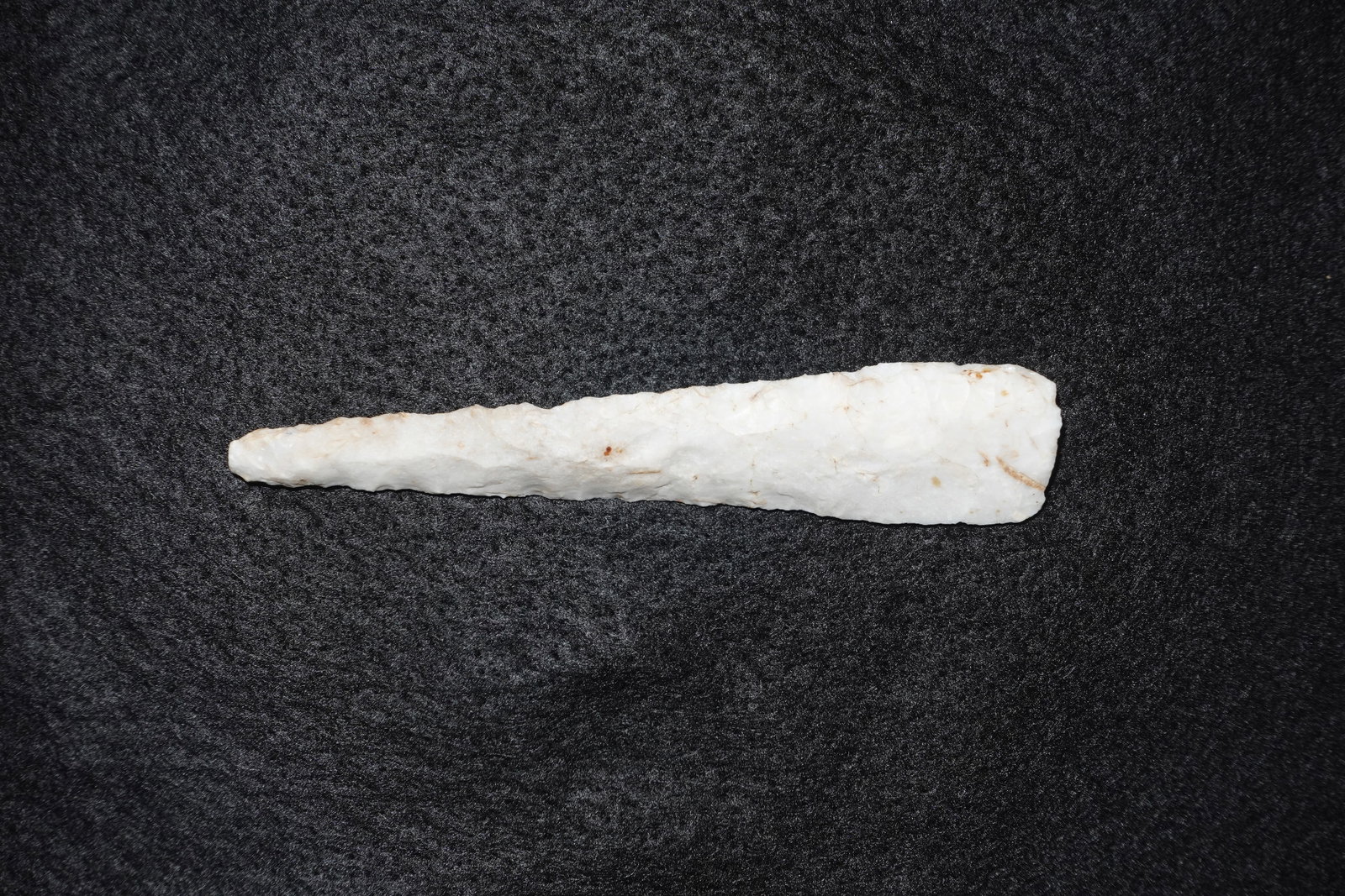 Nebo Hill: Elongated white quartz projectile point with a narrow, tapered profile and bifacial flaking along the edges. One face has a streak of yellow adhesive and handwritten ink markings near the wider base,