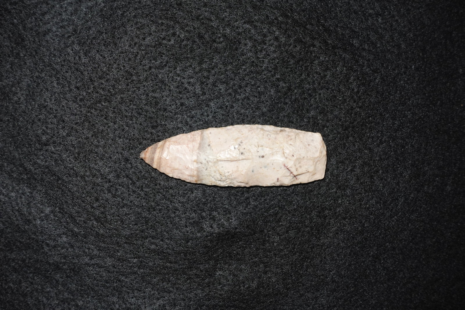 Agate Basin: Lanceolate, bifacial agate projectile point exhibiting fine pressure flake scars and a gently tapered tip. Creamy white to pale pink coloration with subtle banding and scattered dark mineral