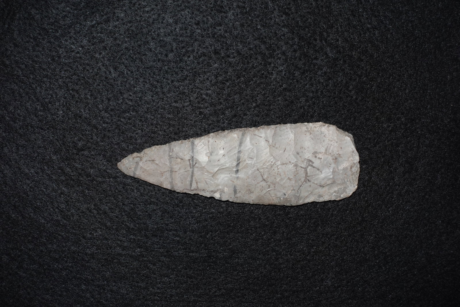 Archaic knife: Bifacial flaked chert blade with a pointed tip and broad, rounded base showing pronounced flake scars across both faces. Light gray to tan coloration with areas of surface patina and scattered residua