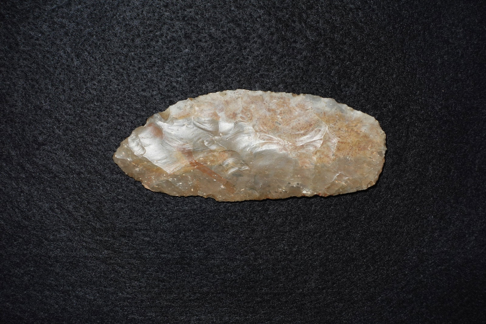 Paleo Knife: Flaked stone knife fashioned from translucent gray-brown chert with extensive bifacial flaking and pronounced rippled flake scars. Elongated, leaf-shaped form with worked margins and tapered ends; sur