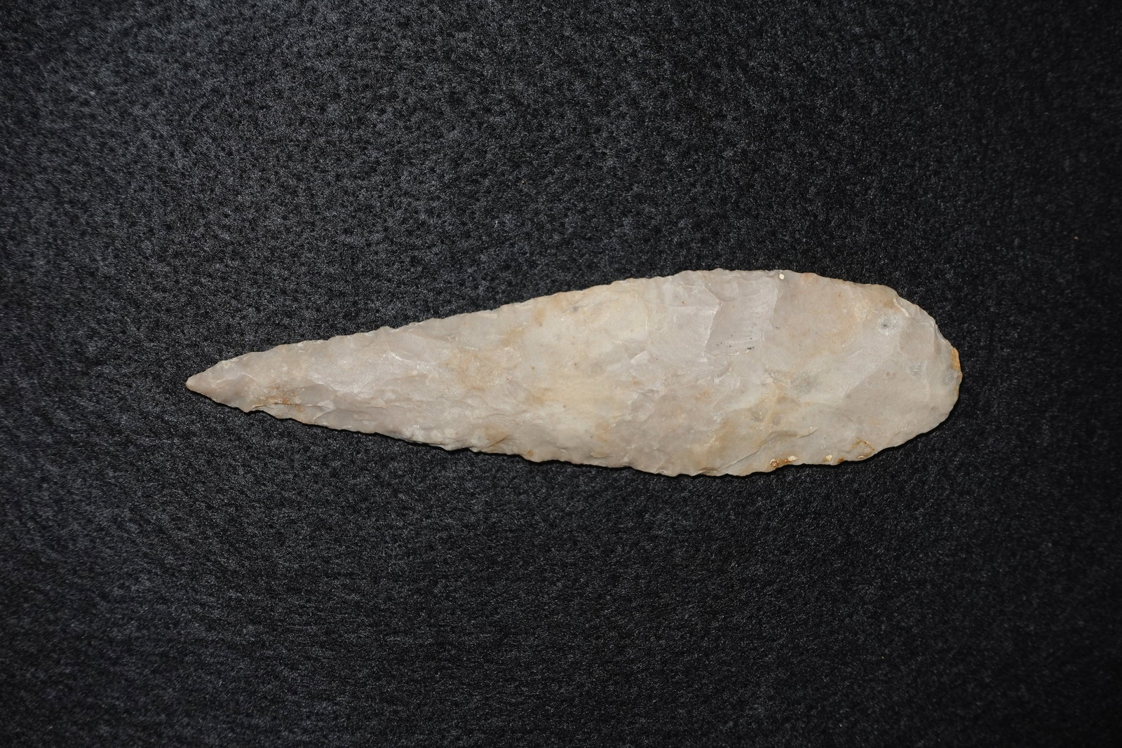 Cobbs: Elongated lanceolate stone projectile point fashioned from translucent milky quartz with cream and tan patches and small iron-stained spots. Bifacial flaking along both faces produces a narrow,
