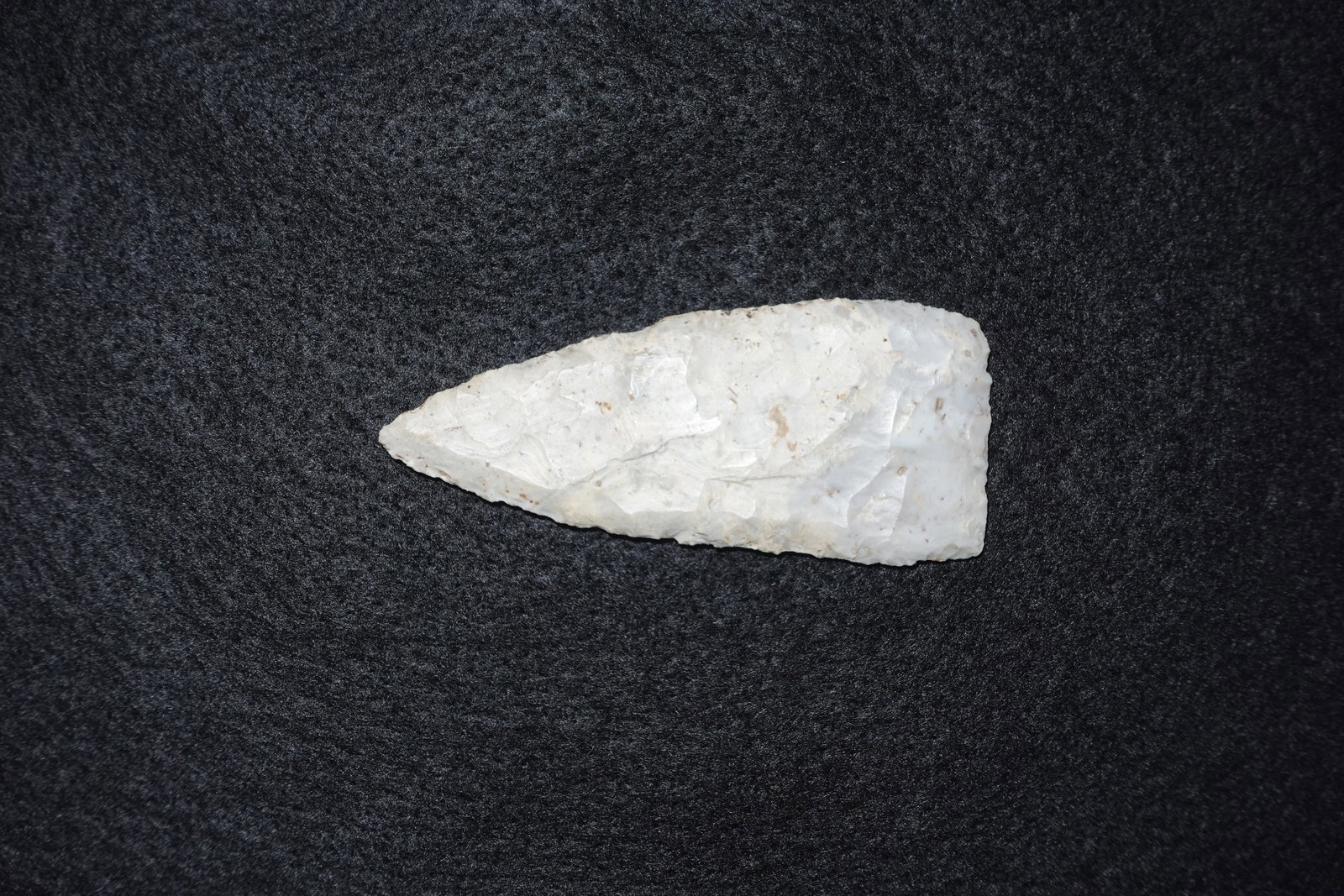 Stanfield: Elongated triangular white translucent flaked stone projectile point with pronounced bifacial thinning and distinct flake scars along the faces. The tip tapers to a narrow point and the base is