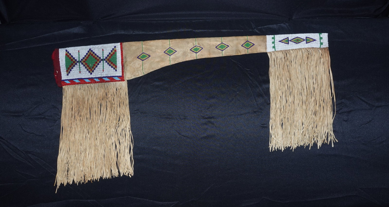 Nez Perce Gun Case: Soft tan hide gun scabbard with long cut-leather fringe and wide white seed-bead cuff panels. Beadwork displays geometric diamond and triangular motifs in green, purple, red, blue and yellow, with