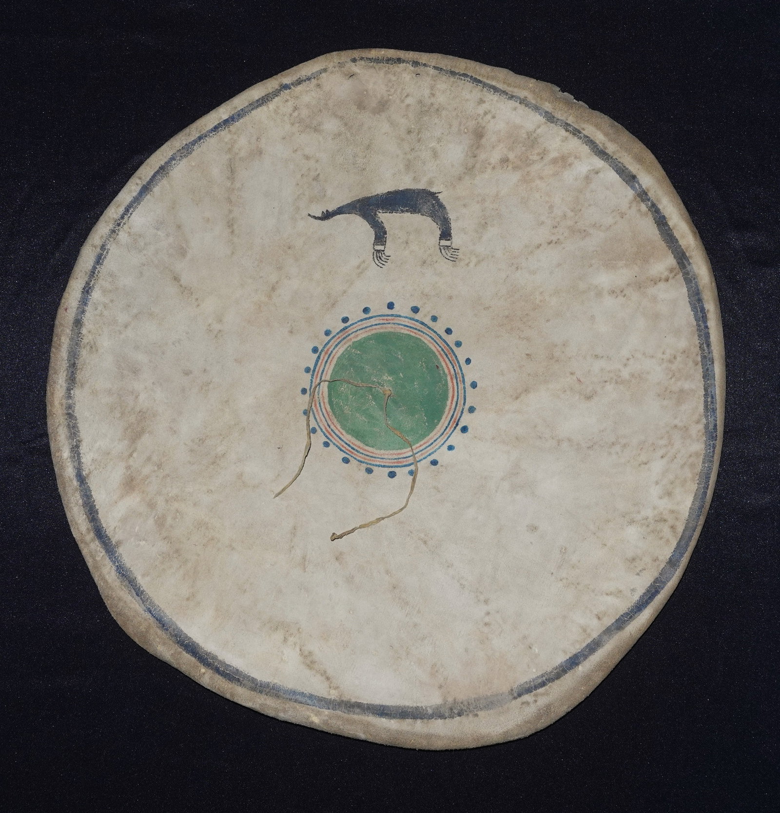 plains Shield Cover: Rawhide cover designed for a circular shield with hand-painted concentric rings in green, blue and red-orange around a central disk. A small black arched motif with fringe-like painted details