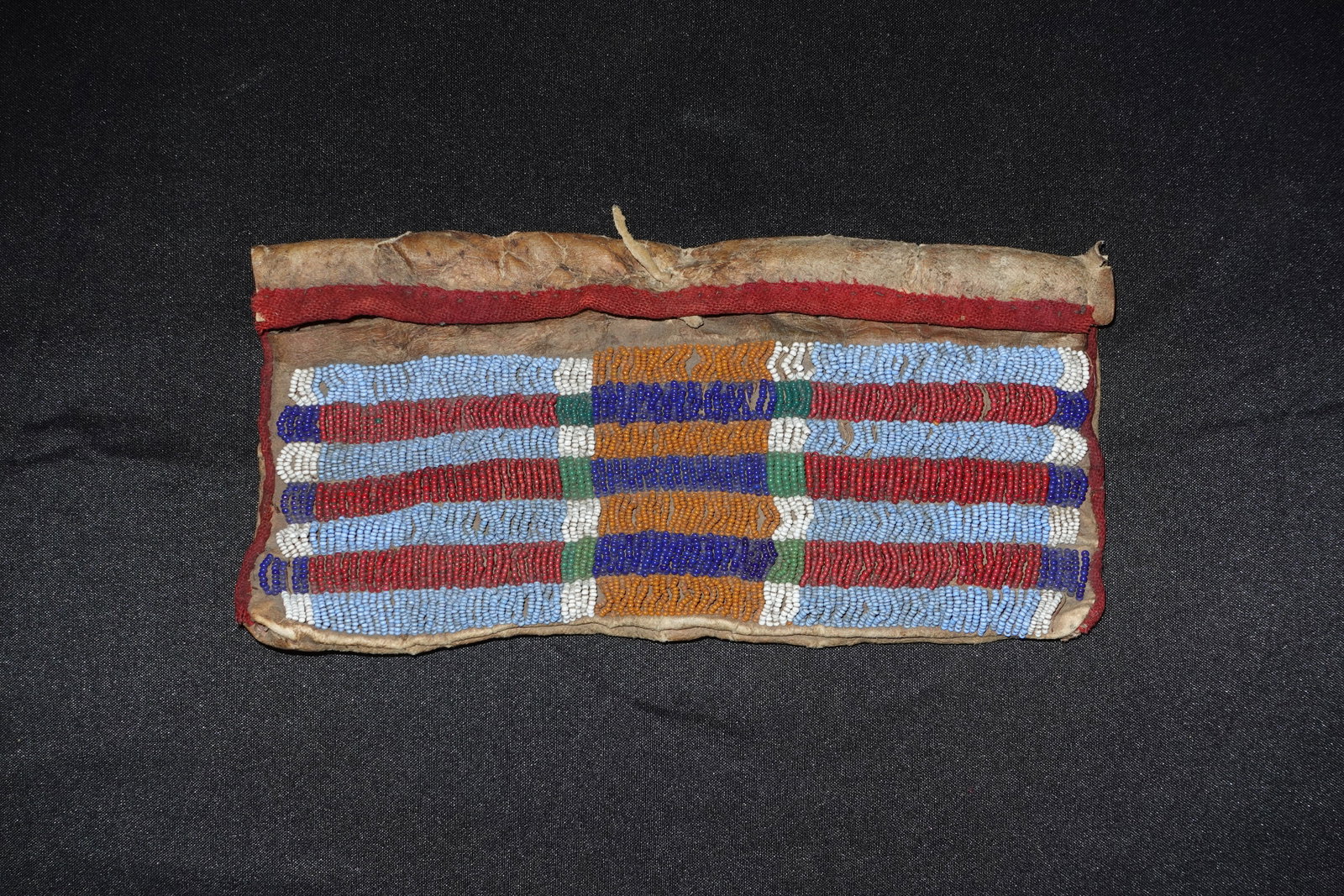 Cheyenne Beaded Bag: Beaded pouch featuring a Cheyenne bar-style pattern worked in glass seed beads in bands of light blue, red, white, navy, green and orange. Fold-over flap constructed from soft tanned hide with a red