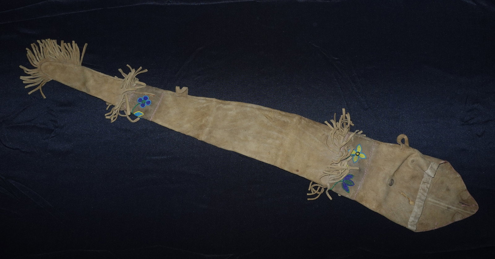 Cree Guncase: Soft tan suede gun case with a long tapered profile and fringed ends. Features hand-stitched seams, a flap with loop closure, and leather tie straps along the body. Decorative glass bead floral